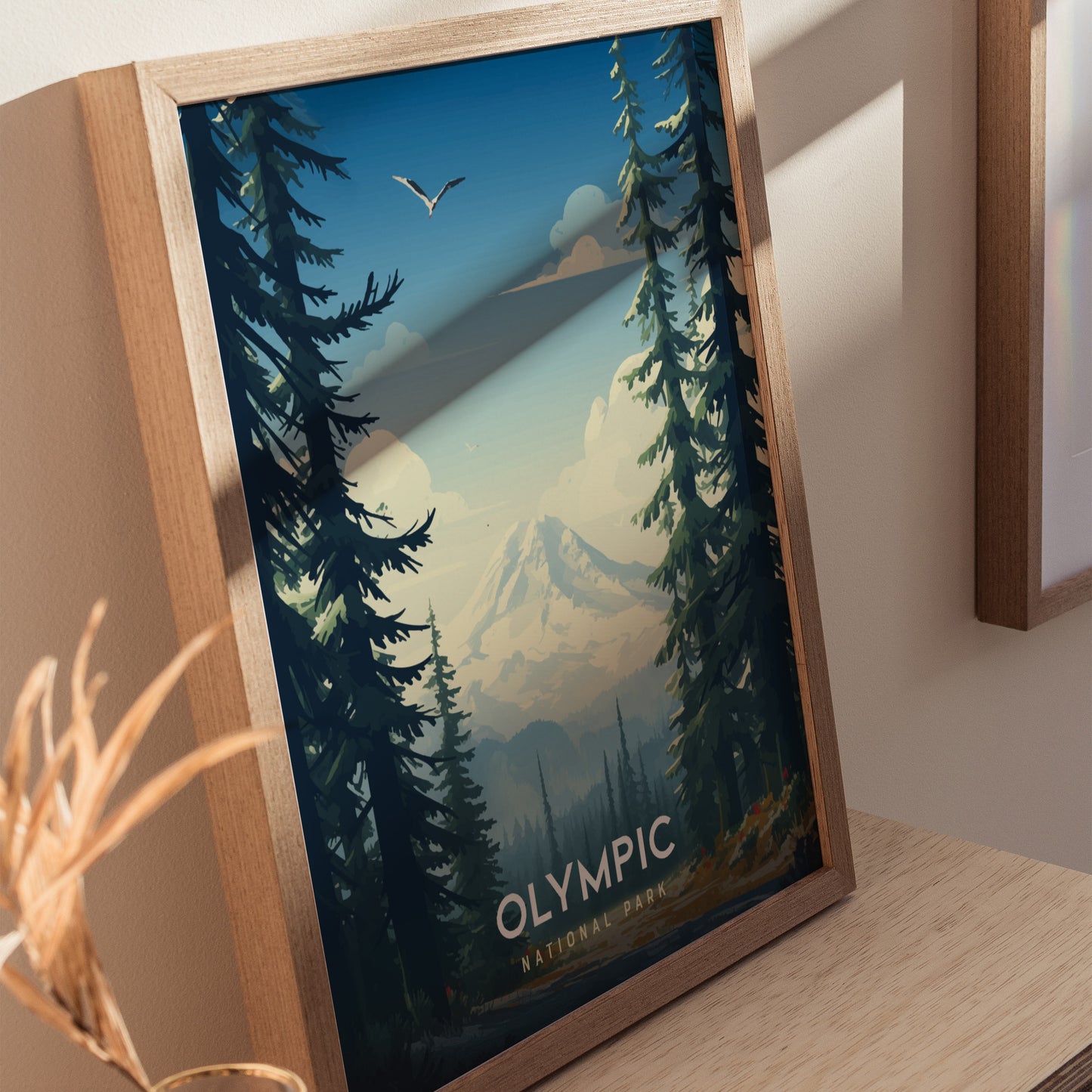Framed artwork of Olympic National Park featuring a mountain, tall evergreen trees, and a bird flying in the sky, displayed on a wooden surface with soft lighting.
