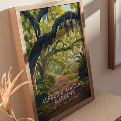A framed poster of Alfred B. Maclay Gardens in Tallahassee, Florida, features vibrant moss-draped trees over a winding brick path, displayed on a wooden surface with soft lighting.