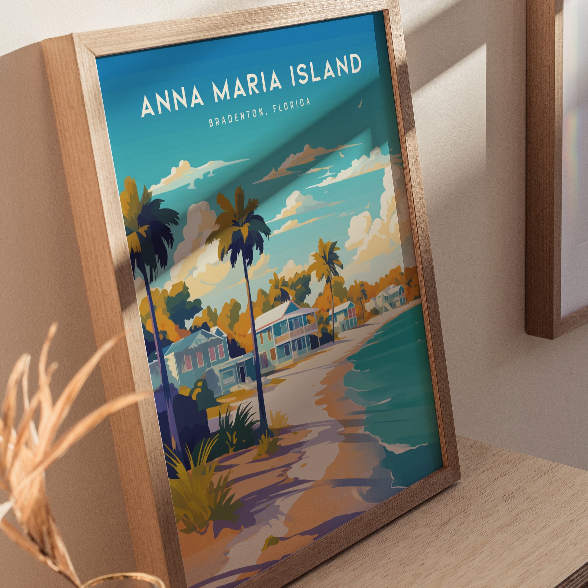 The image shows a framed Anna Maria Island poster featuring colorful beach cottages, palm trees, and a serene shoreline under a vibrant sky. The artwork rests on a wooden surface, adding a warm touch.