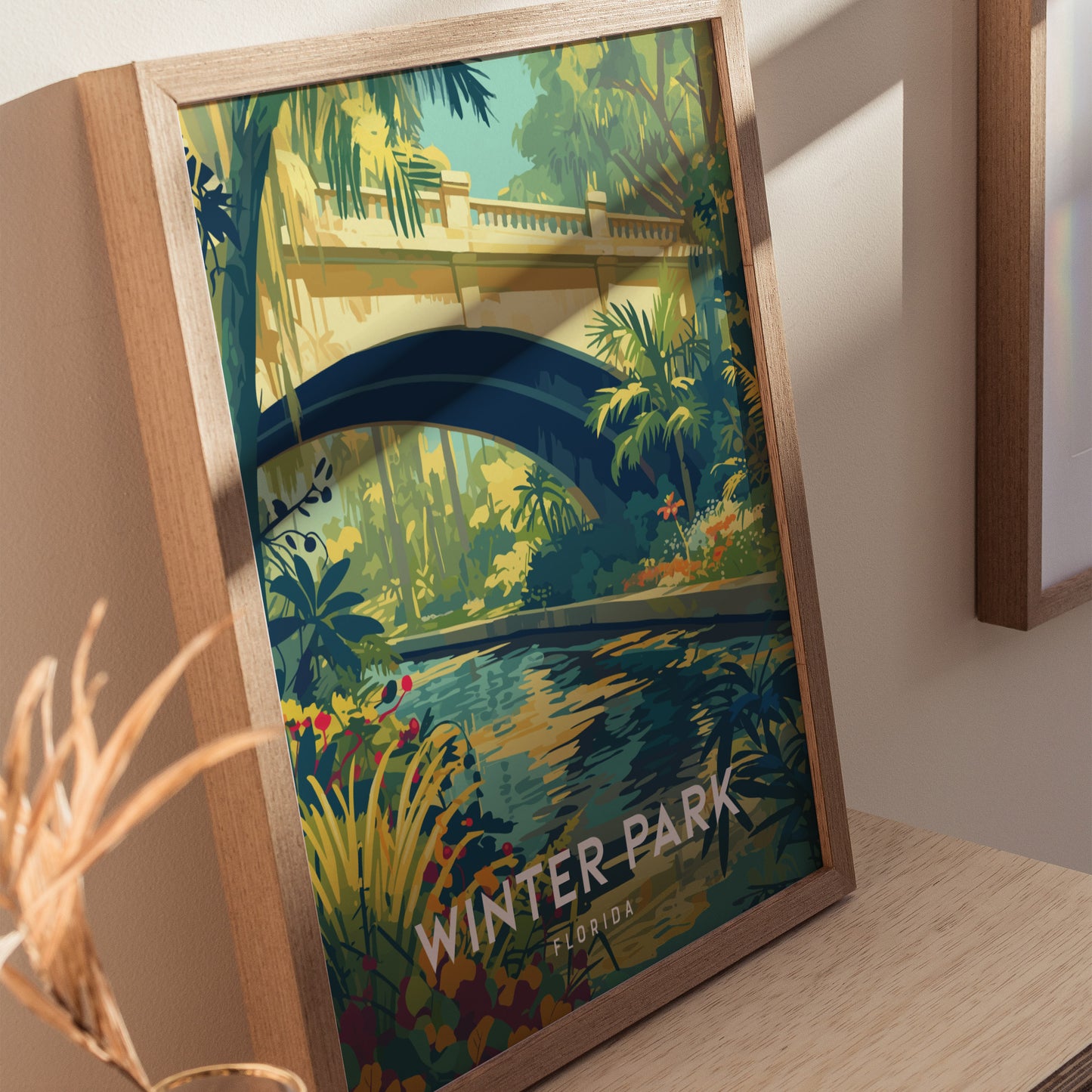A framed poster depicting a lush garden with a stream flowing beneath an arched bridge, surrounded by tropical plants. The text Winter Park Florida is visible at the bottom.