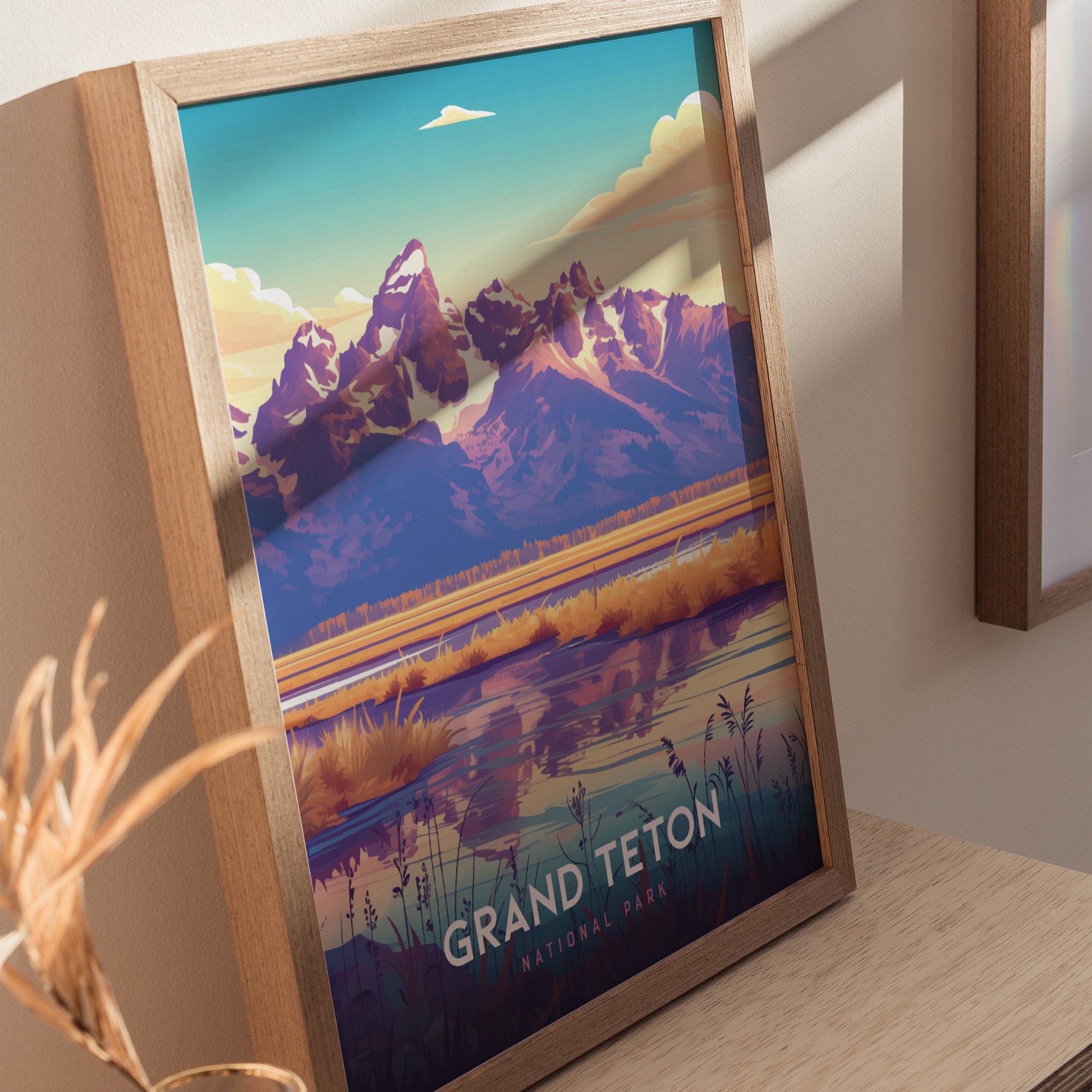 Framed artwork of Grand Teton National Park featuring vibrant mountains and a mirrored lake, displayed on a wooden surface. Bright colors and natural light enhance the visual appeal.