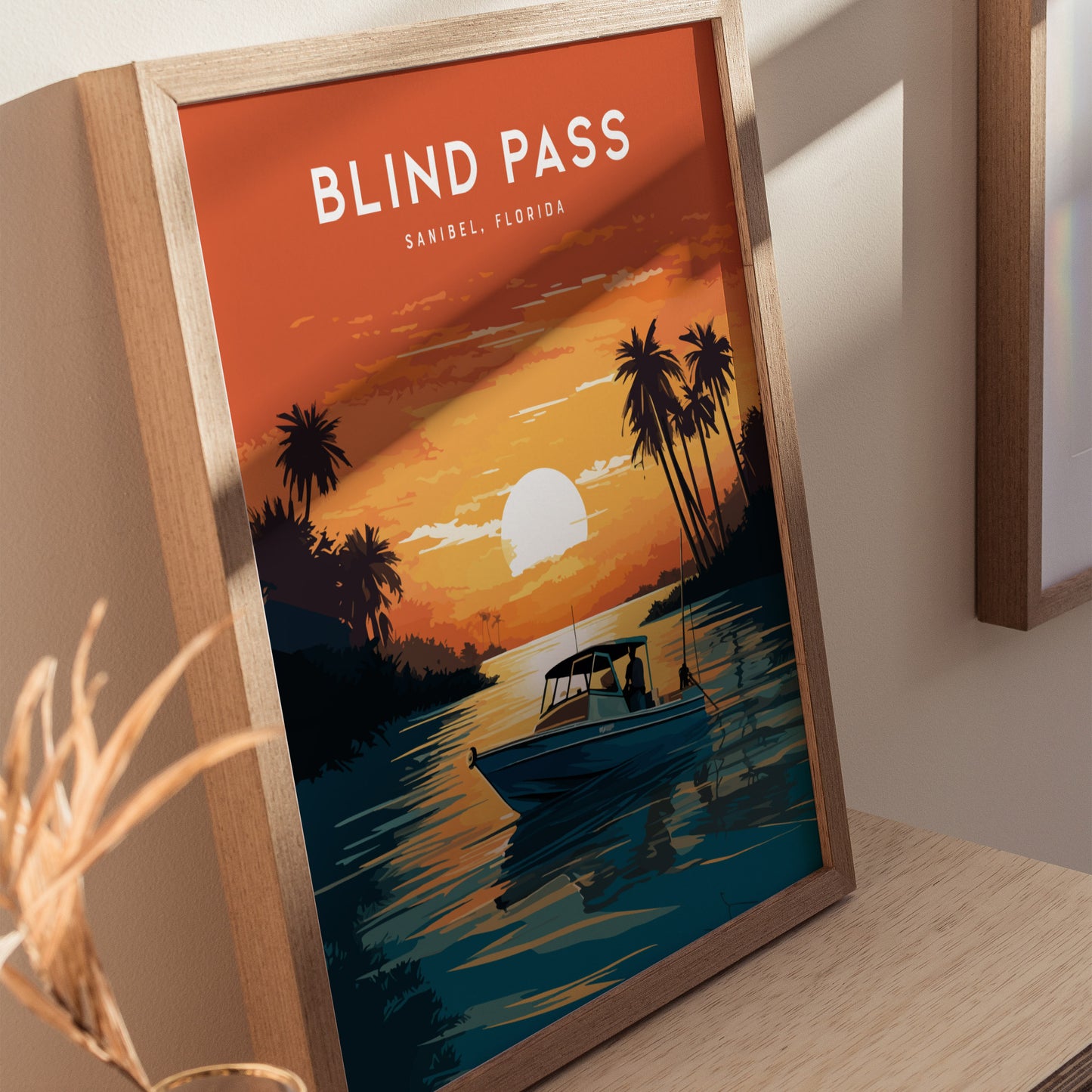 Framed artwork titled Blind Pass Sanibel, Florida depicts a sunset scene with palm trees and a boat on water. The warm orange and yellow hues create a tranquil atmosphere.
