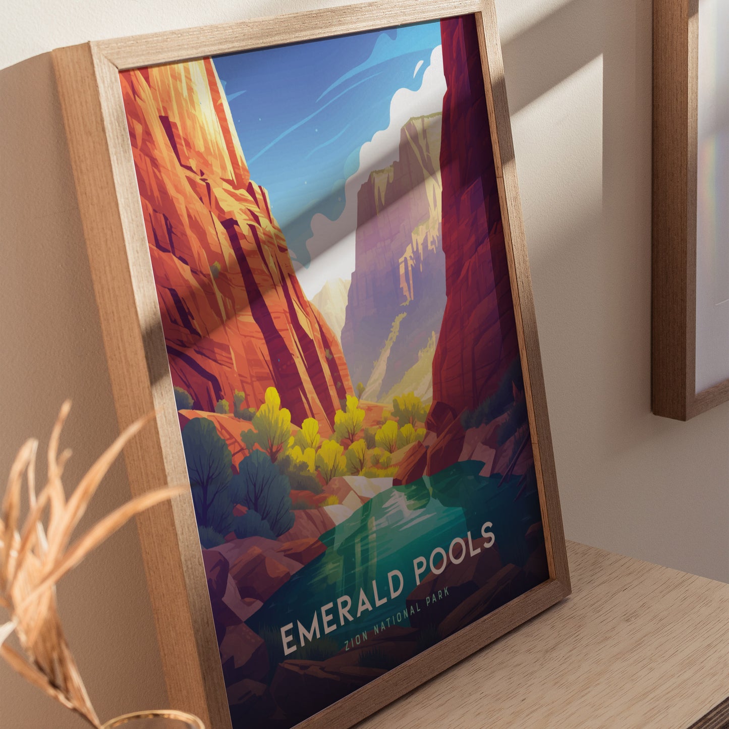 Framed poster of Zion National Parks Emerald Pools, featuring vibrant red cliffs, lush greenery, and a serene blue sky. Displayed on a wooden surface.