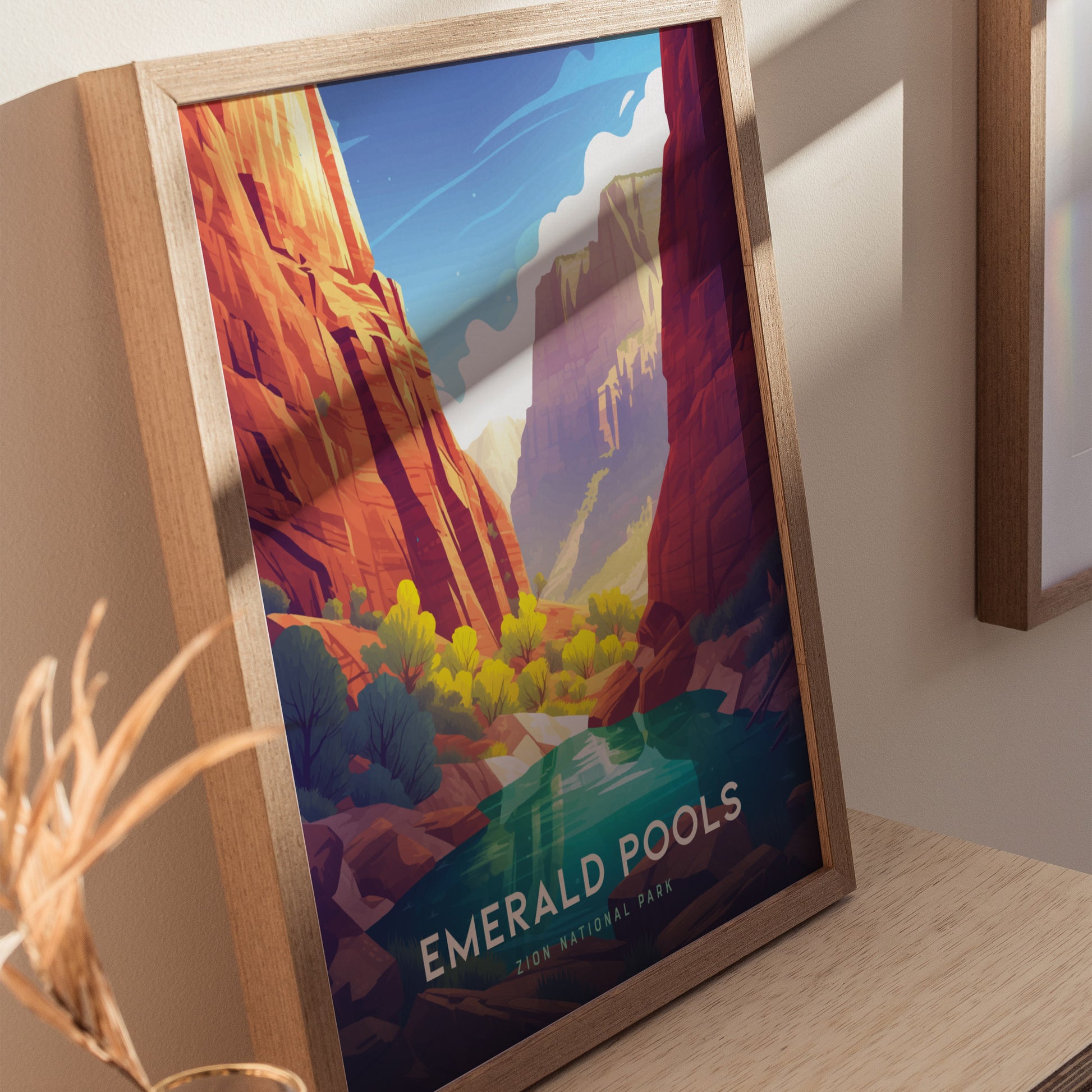 Framed poster of Zion National Parks Emerald Pools, featuring vibrant red cliffs, lush greenery, and a serene blue sky. Displayed on a wooden surface.