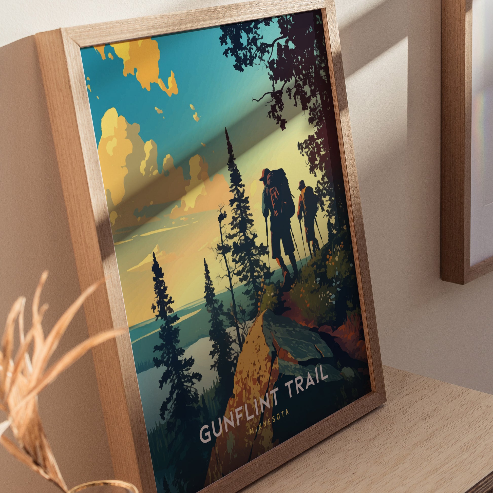A framed poster depicts hikers with backpacks on a scenic trail surrounded by trees and a vibrant sunset sky, labeled Gunflint Trail, Minnesota.