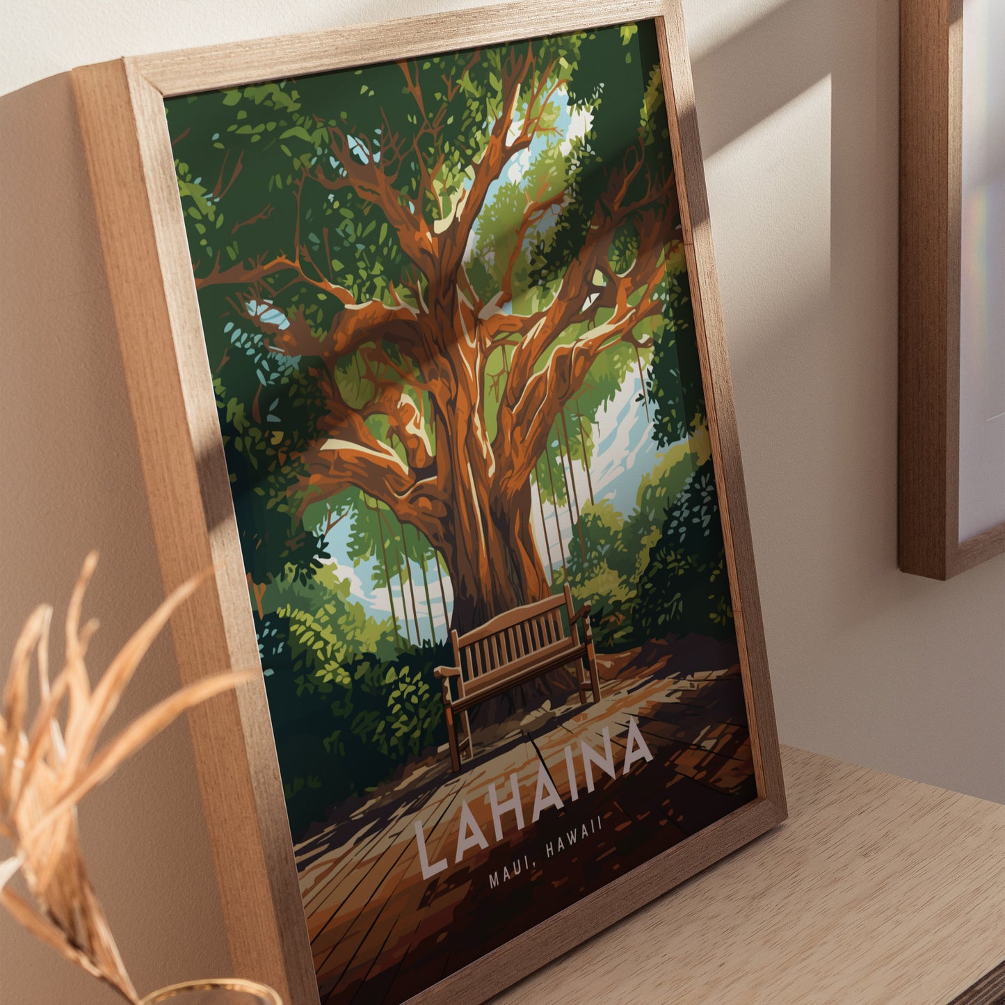 Framed poster of a vibrant banyan tree with a wooden bench underneath, labeled Lahaina, Maui, Hawaii. The artwork is displayed on a wooden surface, casting soft shadows.