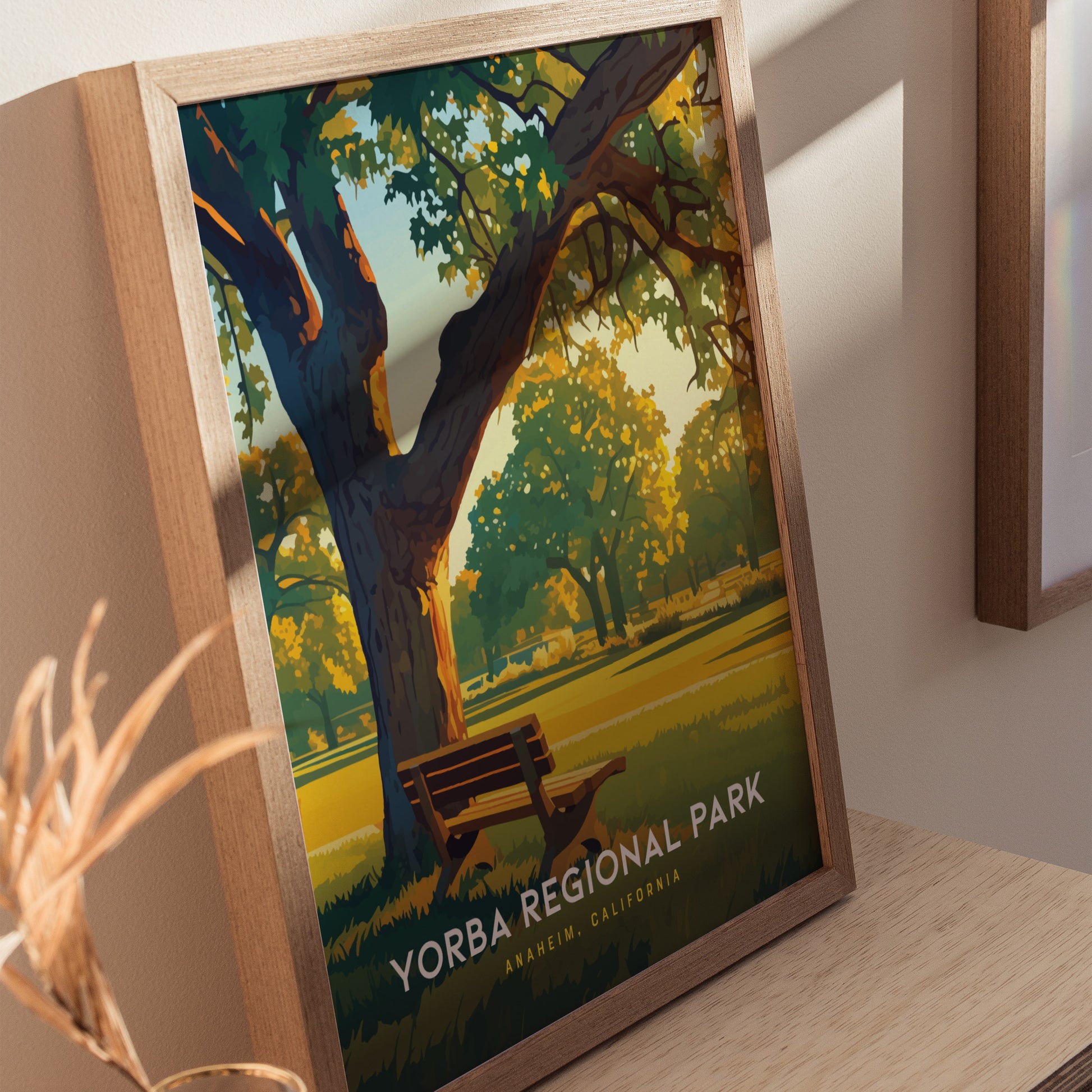 Framed poster of Yorba Regional Park featuring a sunlit path lined with trees and a wooden bench, displayed on a wooden surface. Tranquil outdoor setting with vibrant colors.