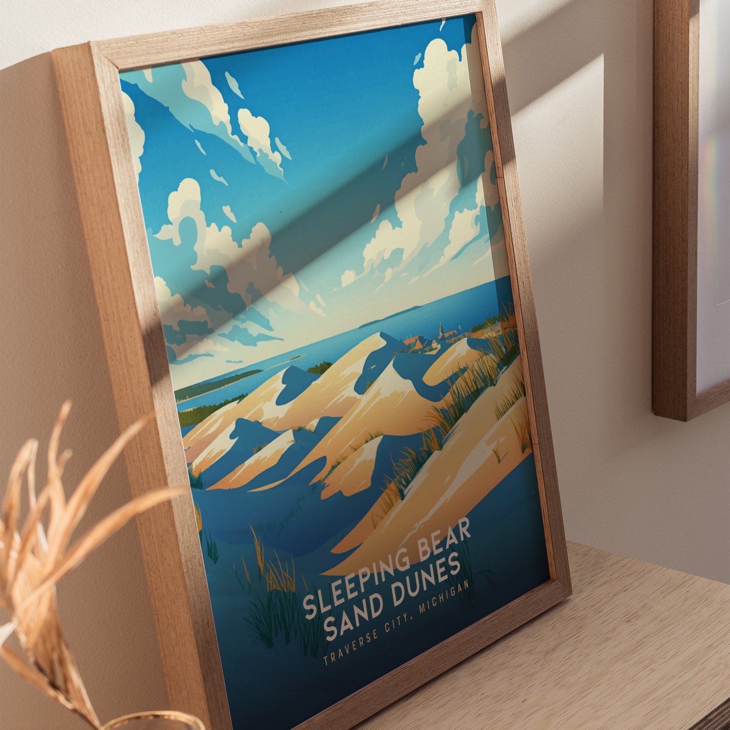A framed poster of Sleeping Bear Sand Dunes features golden dunes under a vibrant blue sky with clouds, set against a distant view of Lake Michigan.