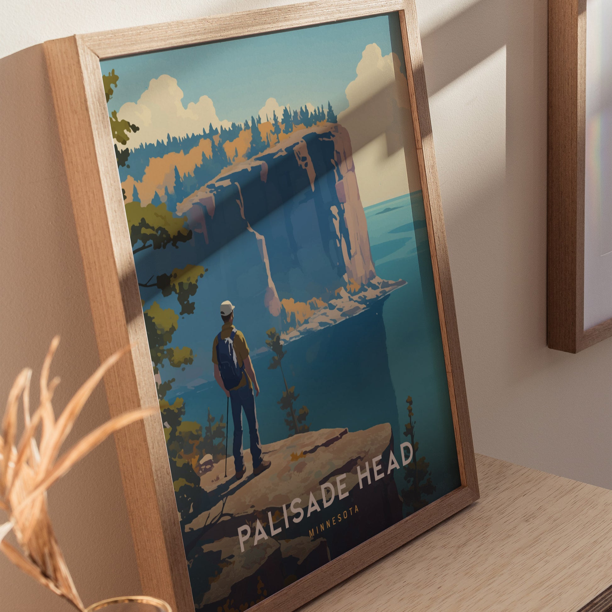 Framed artwork featuring a hiker overlooking Palisade Heads cliffs with a vibrant landscape, displayed on a wooden surface. The poster highlights Minnesotas scenic beauty.