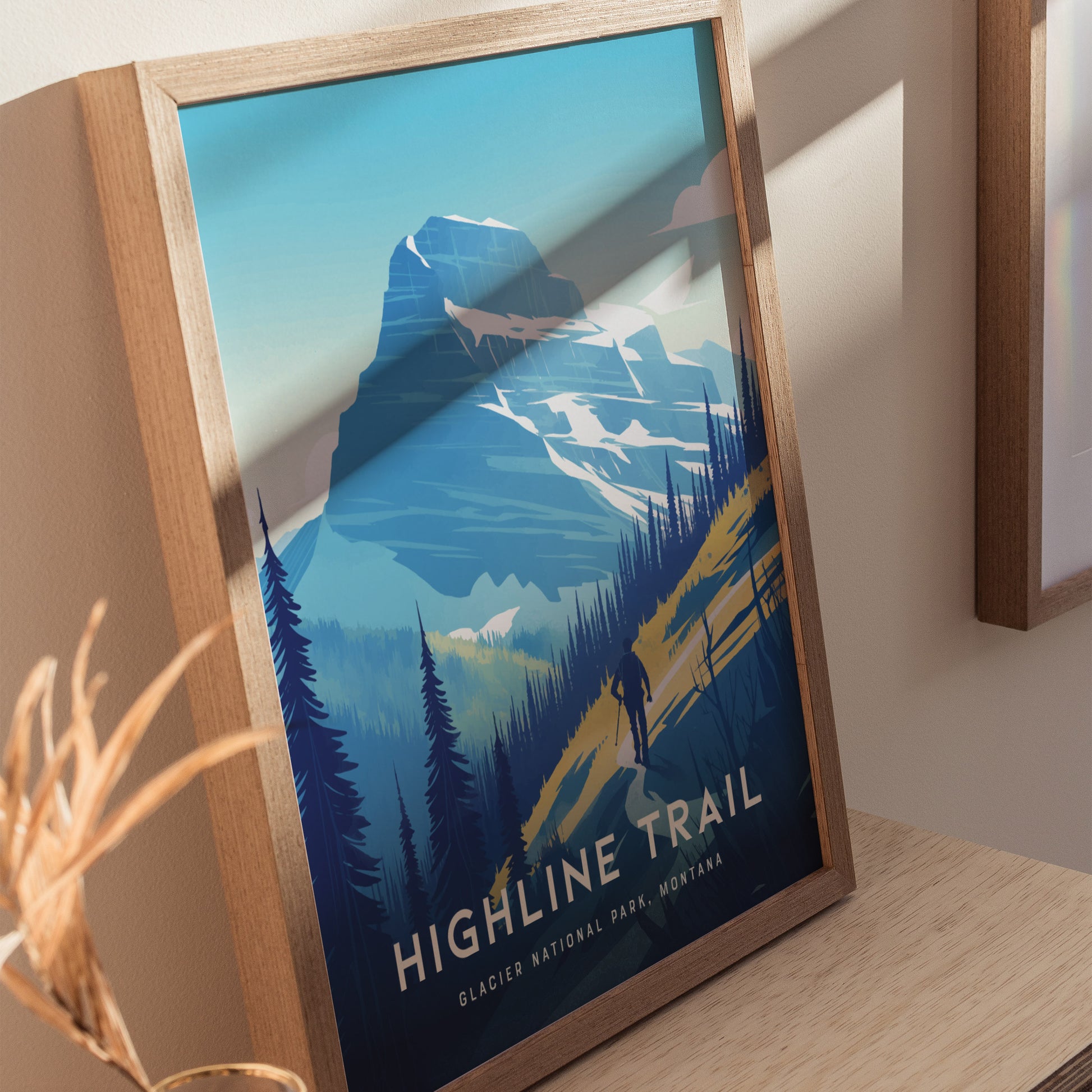 A framed poster of the Highline Trail in Glacier National Park, featuring a hiker silhouette against a backdrop of mountains and pine trees under a clear blue sky.