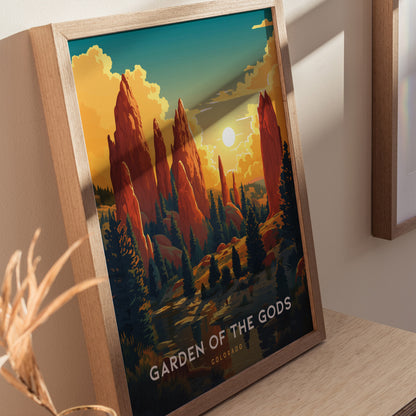 Framed poster of Garden of the Gods featuring vivid red rock formations, pine trees, and a setting sun. The artwork is displayed on a wooden surface with natural lighting.