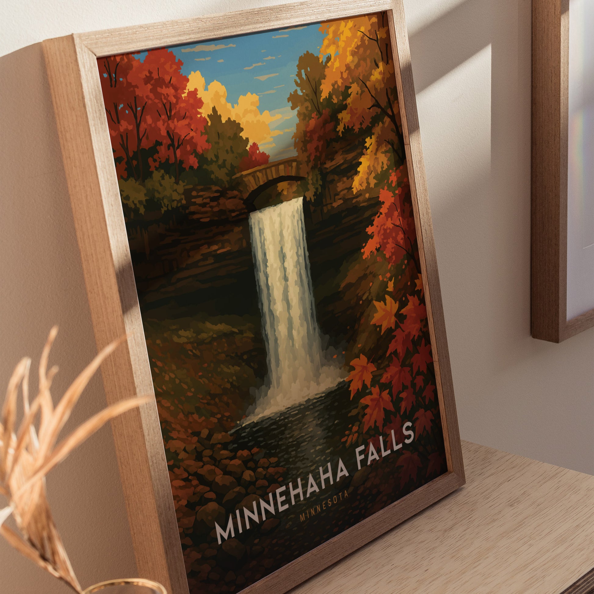 Framed poster of Minnehaha Falls, featuring a waterfall with vibrant autumn foliage and a stone bridge, set against a blue sky with clouds. Text reads Minnehaha Falls, Minnesota.