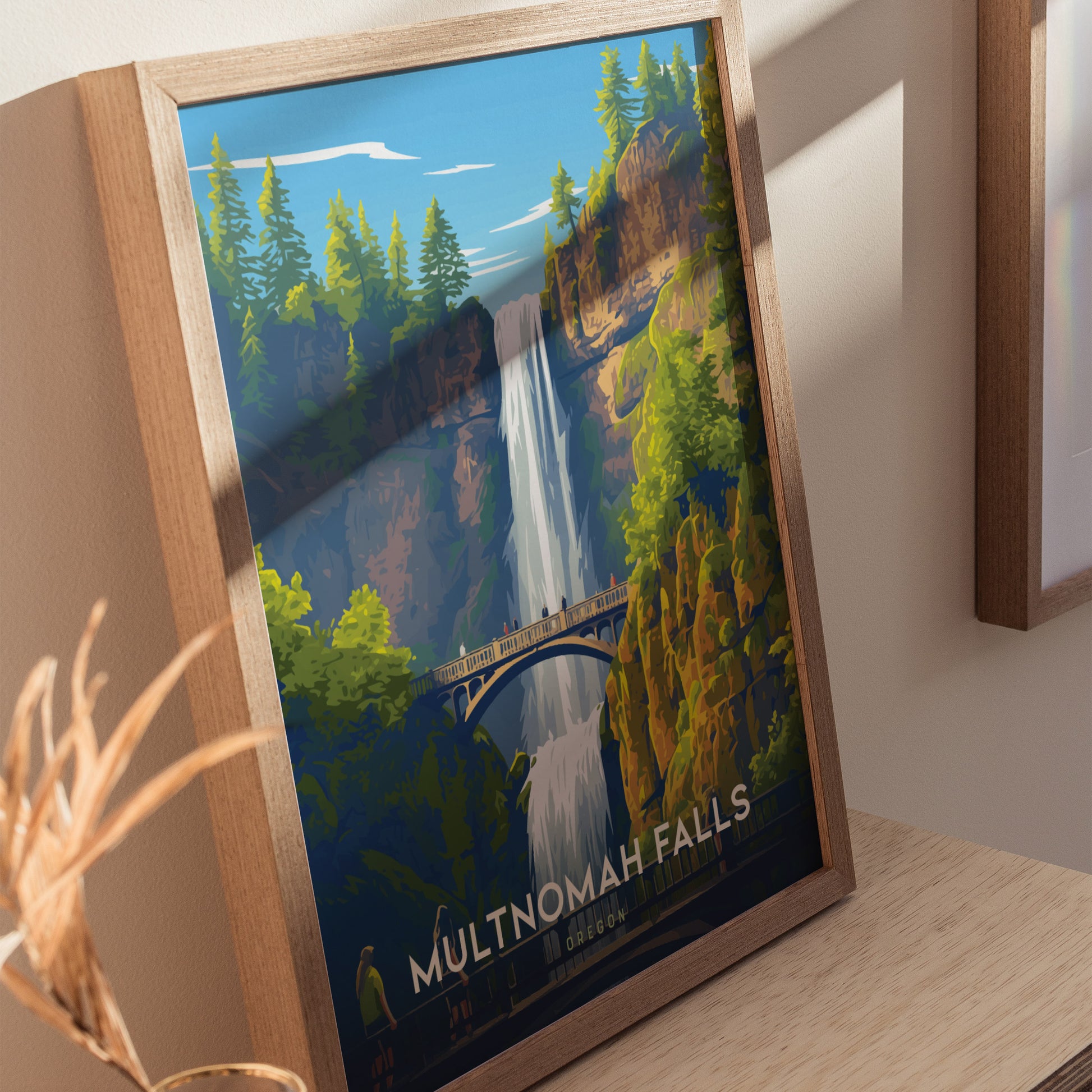 Framed poster of Multnomah Falls, depicting a vibrant waterfall, lush green trees, and the iconic Benson Bridge under a clear blue sky. Displayed on a wooden surface.