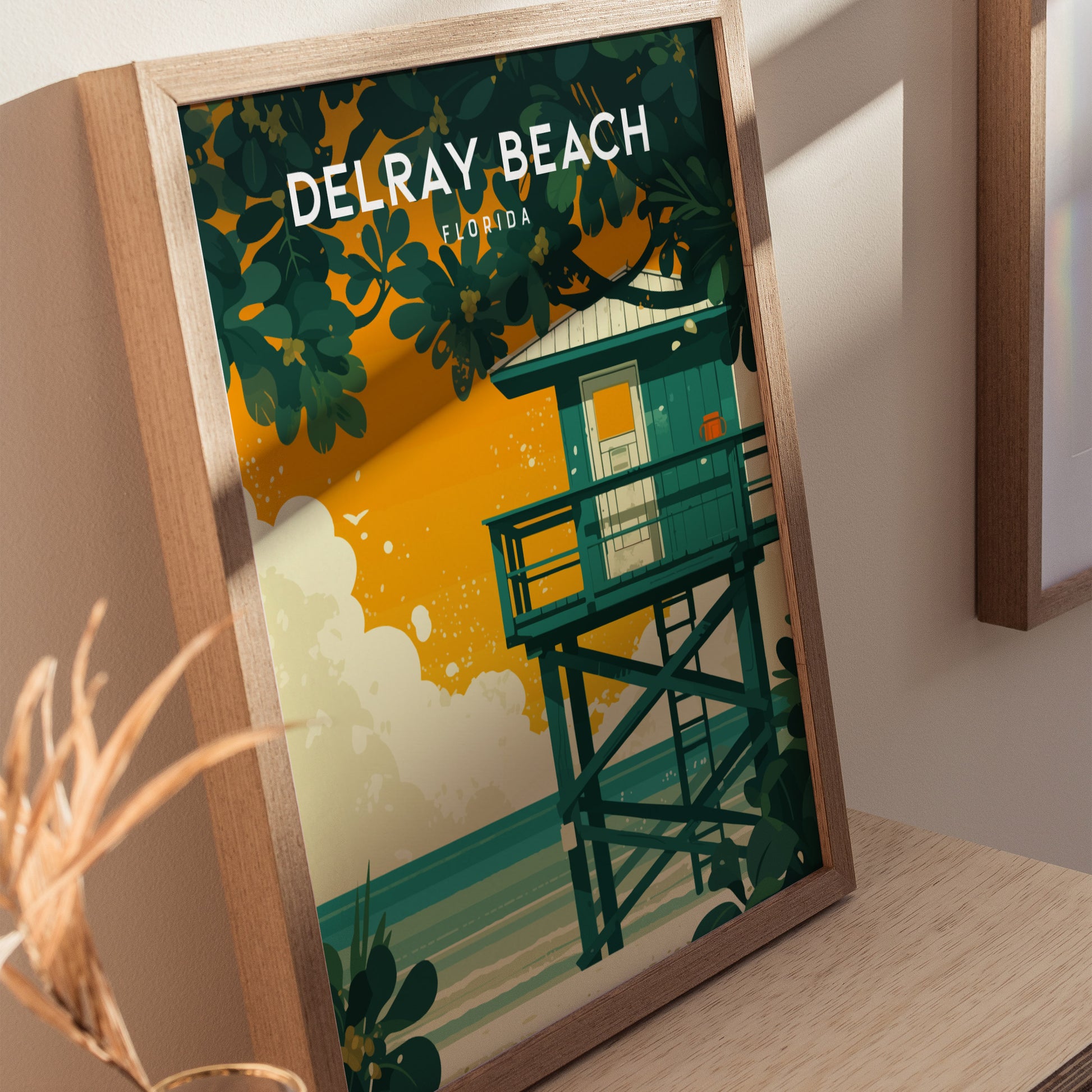A framed Delray Beach poster features a vibrant illustration of a lifeguard stand with lush sea grape leaves against an orange sky. The words Delray Beach Florida are visible.