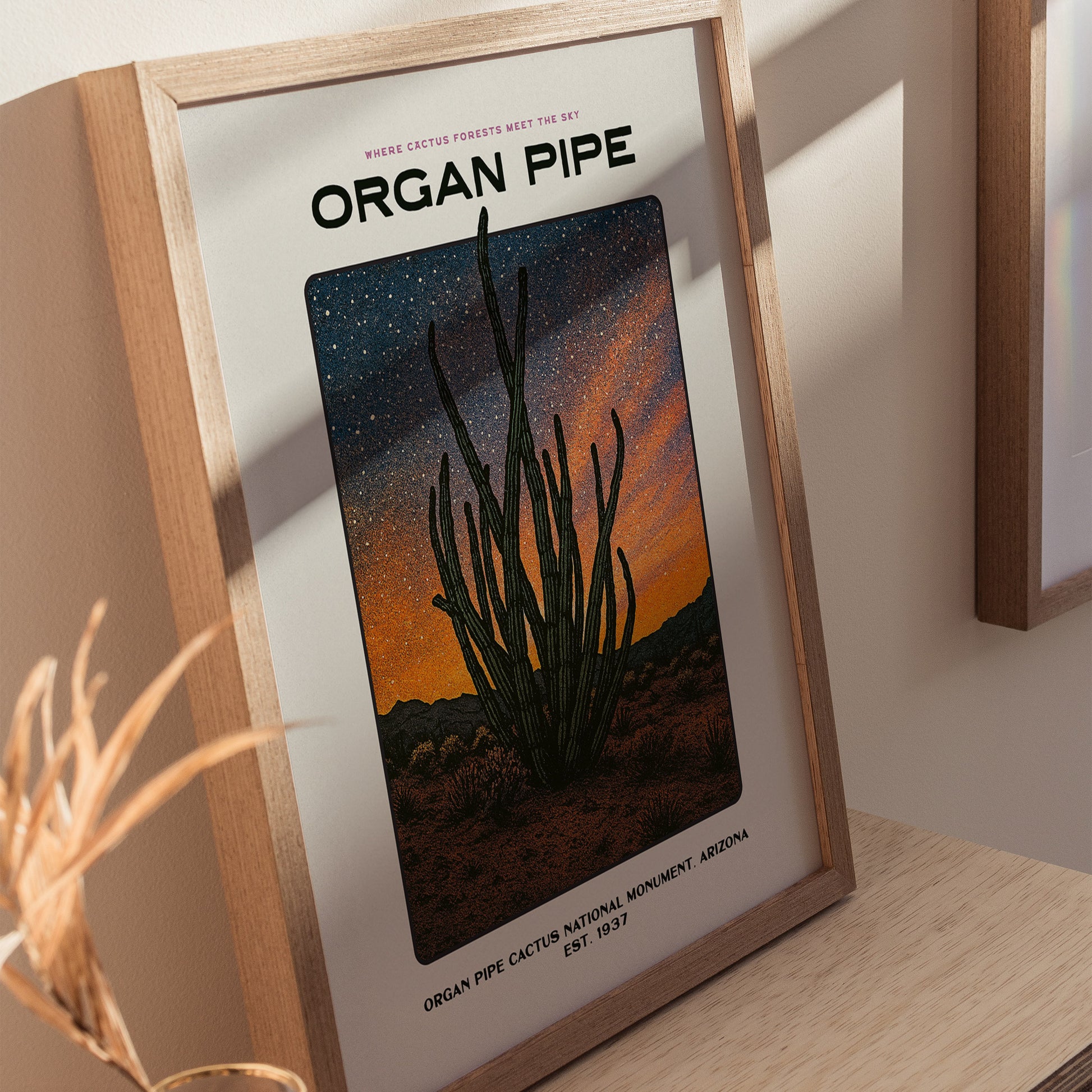 Natural wood framed Organ Pipe Cactus poster leaning on a shelf next to indoor plants and decorative ceramics
