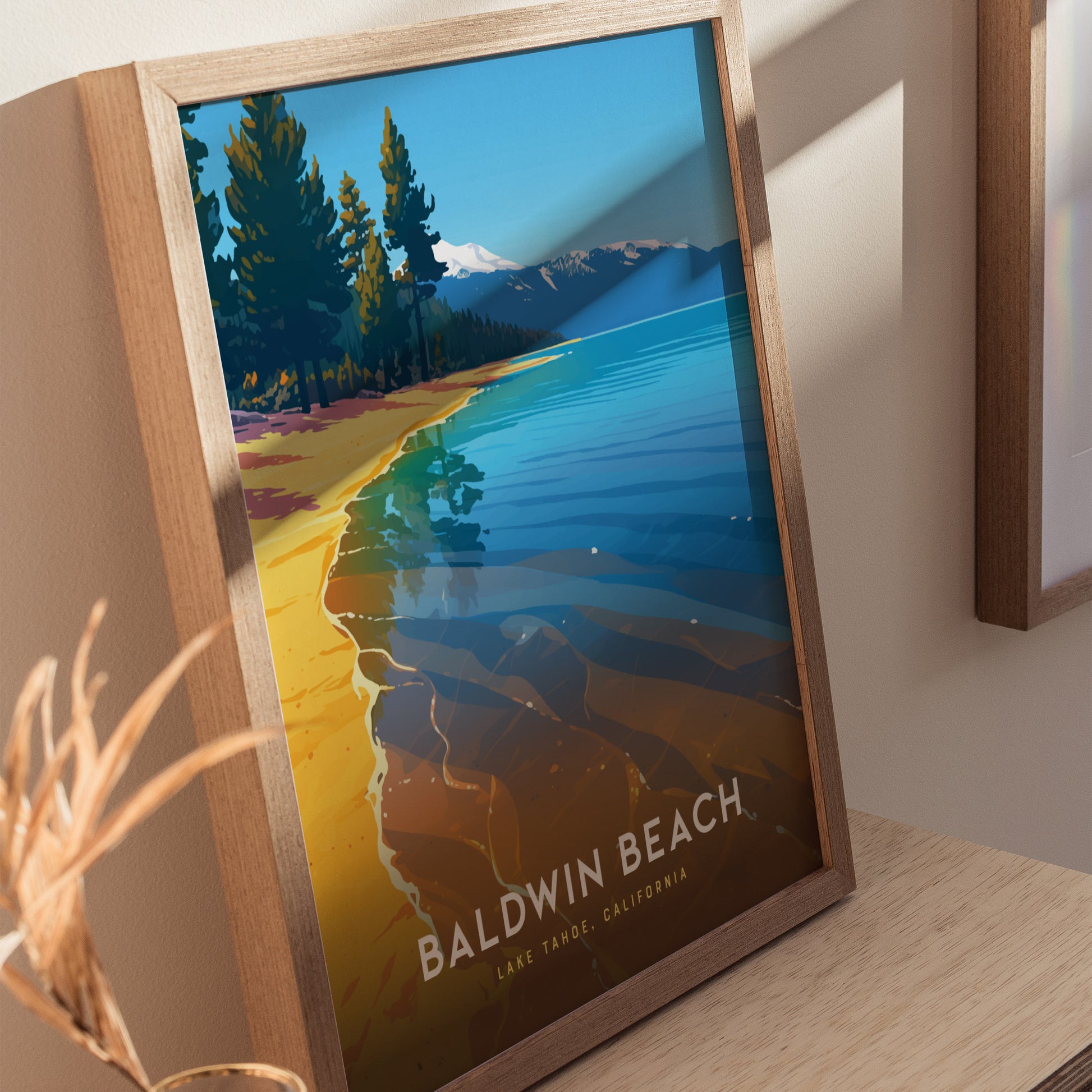 Framed poster of Baldwin Beach, Lake Tahoe, featuring vibrant blue waters, sandy shores, and a pine tree-lined landscape with distant mountains. Displayed on a wooden table with soft lighting.