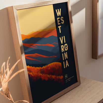 Framed poster of West Virginia featuring abstract, layered mountains in warm oranges and cool blues, with bold text on the side. Displayed on a wooden surface with natural lighting.