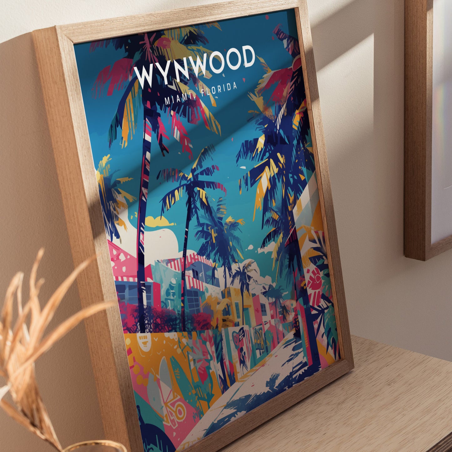 A framed poster titled Wynwood Miami Florida depicts vibrant street art with colorful graffiti and tall palm trees under a bright blue sky. The artwork captures the lively and creative atmosphere of Miamis art district.