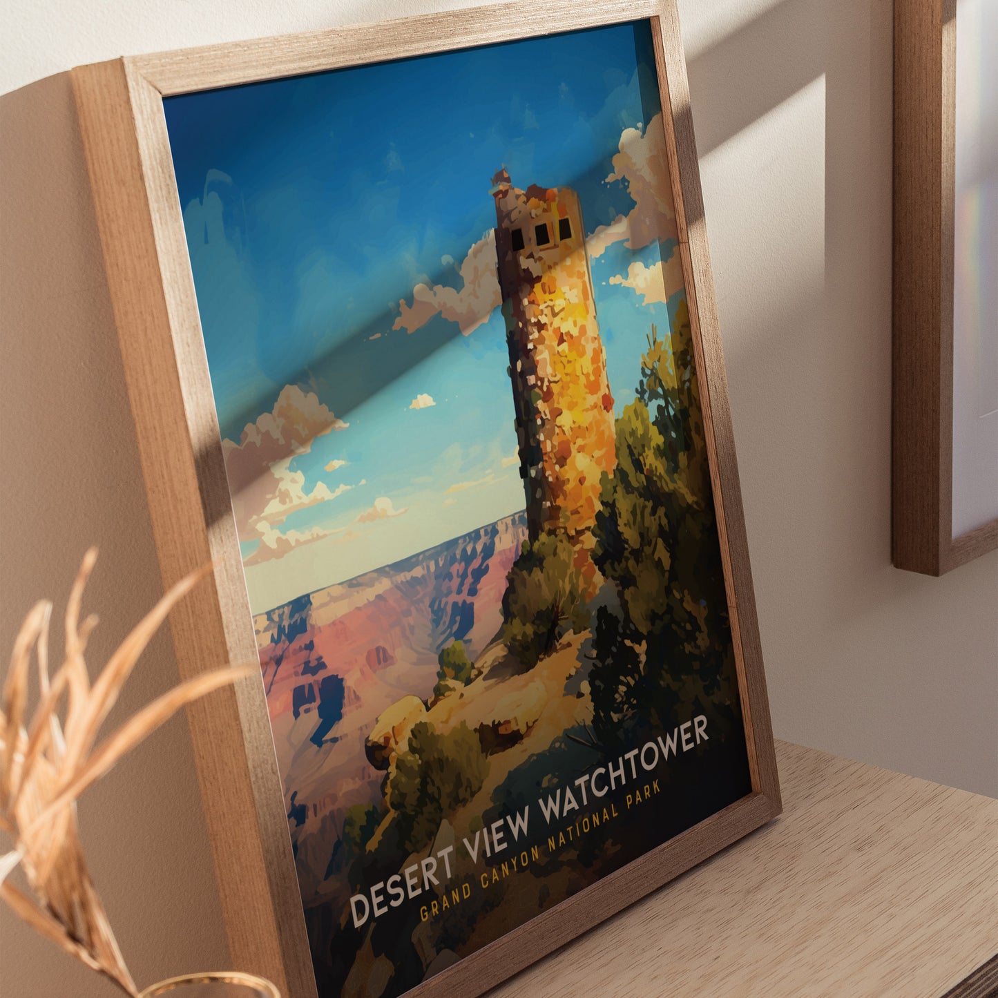 Framed poster depicting the Desert View Watchtower at Grand Canyon National Park, featuring a stone tower against a vibrant blue sky with clouds. Displayed on a wooden surface.