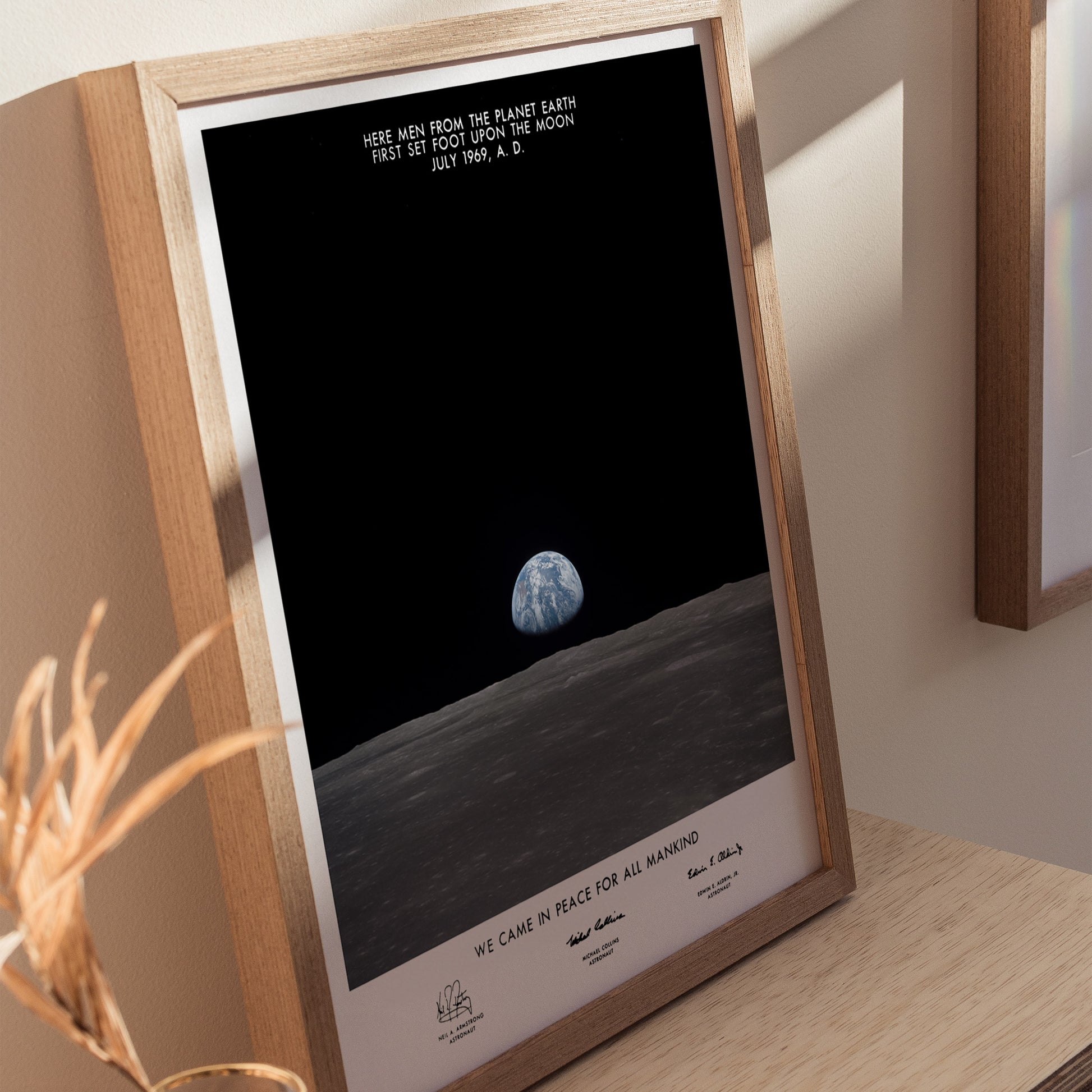 Framed print of a lunar landing poster with text on a wooden surface.
