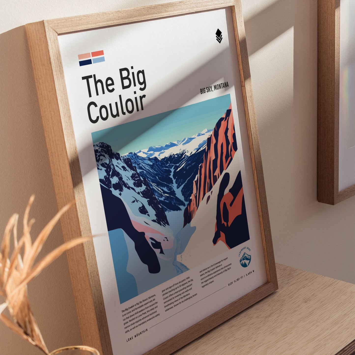 Framed poster of The Big Couloir at Big Sky, Montana, featuring an illustrated ski run with snowy mountains and rugged terrain. Sunlight casts shadows on the wooden surface.