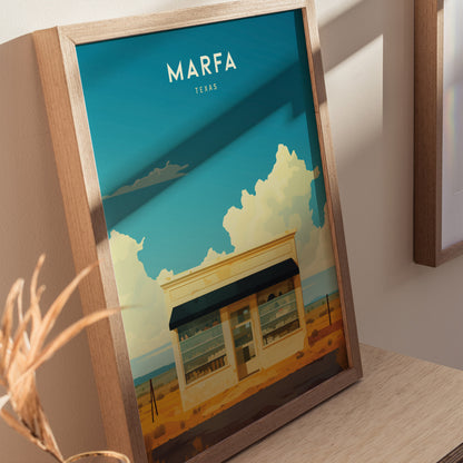 Framed poster depicting a desert art installation with a small building under a vast blue sky and fluffy clouds, labeled Marfa Texas at the top.