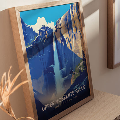 A framed poster of Upper Yosemite Falls with vibrant blue and orange hues, depicting the waterfall cascading down granite cliffs, is displayed on a wooden surface.