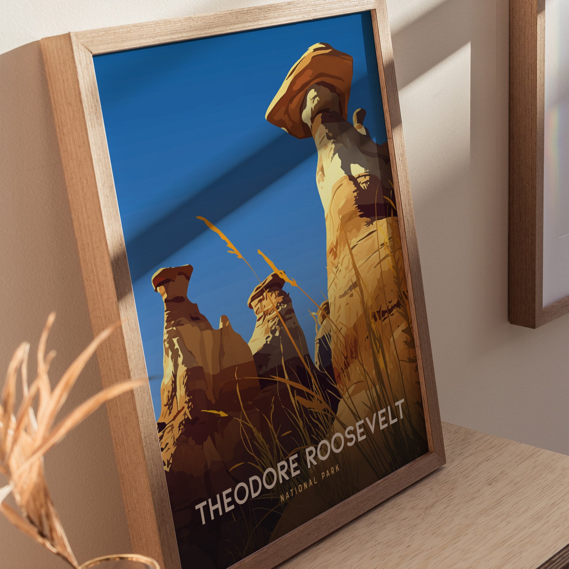 A framed poster depicts the striking hoodoos of Theodore Roosevelt National Park against a clear blue sky, with tall grasses in the foreground. The text reads Theodore Roosevelt National Park.