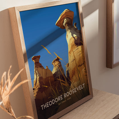 A framed poster depicts the striking hoodoos of Theodore Roosevelt National Park against a clear blue sky, with tall grasses in the foreground. The text reads Theodore Roosevelt National Park.