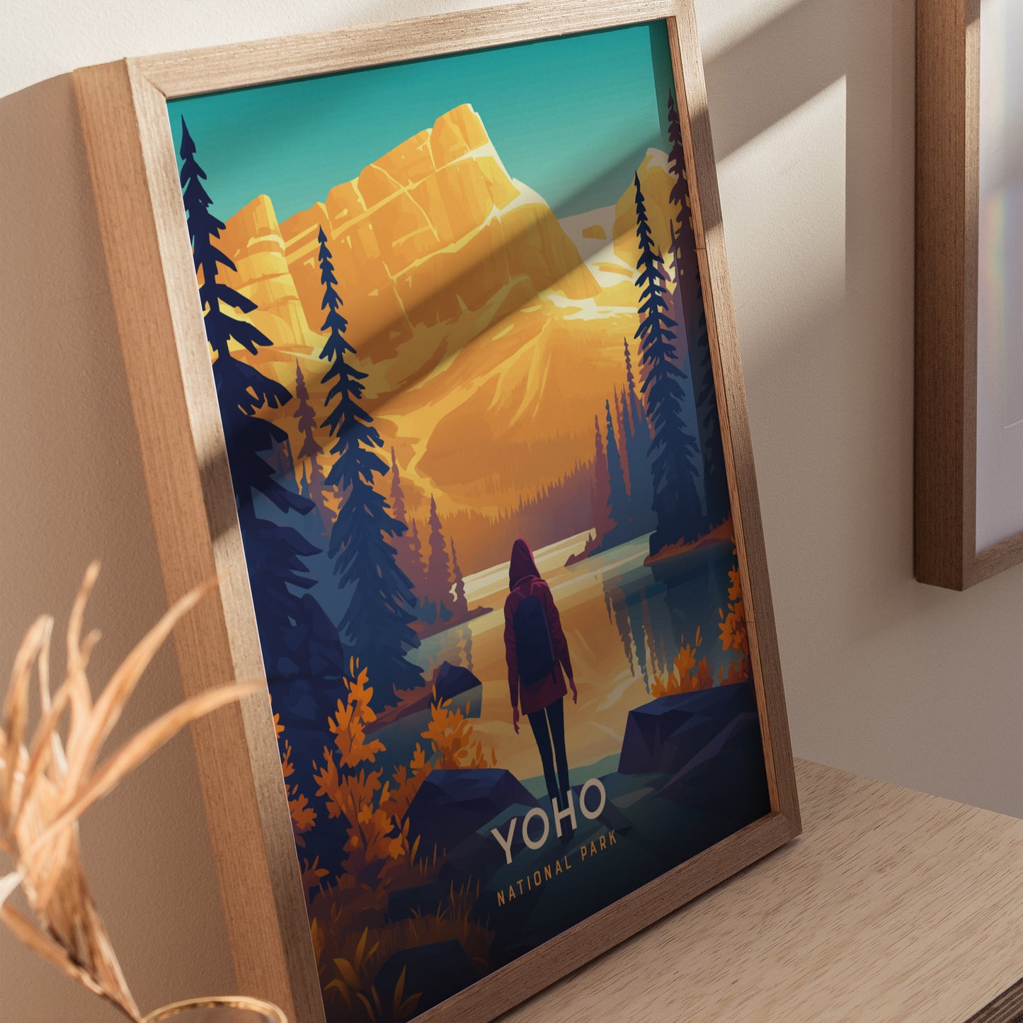 A framed poster features a stylized illustration of Yoho National Park with a hiker, towering trees, and majestic mountains under a vibrant sky. The text reads Yoho National Park.