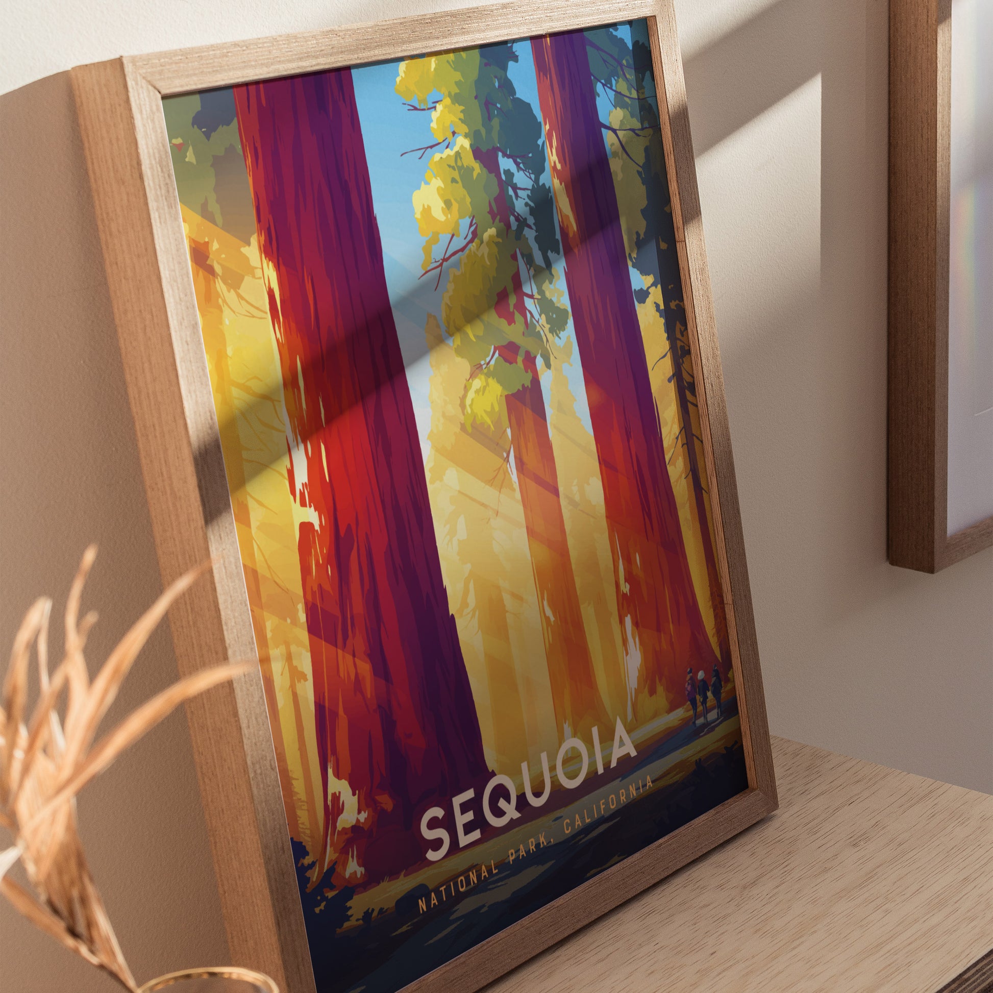 Framed poster featuring vibrant artwork of towering sequoia trees with sunlight filtering through, labeled Sequoia National Park, California, resting on a wooden surface.