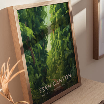Framed poster titled Fern Canyon shows lush, green canyon walls covered in ferns, placed on a wooden surface with soft lighting.