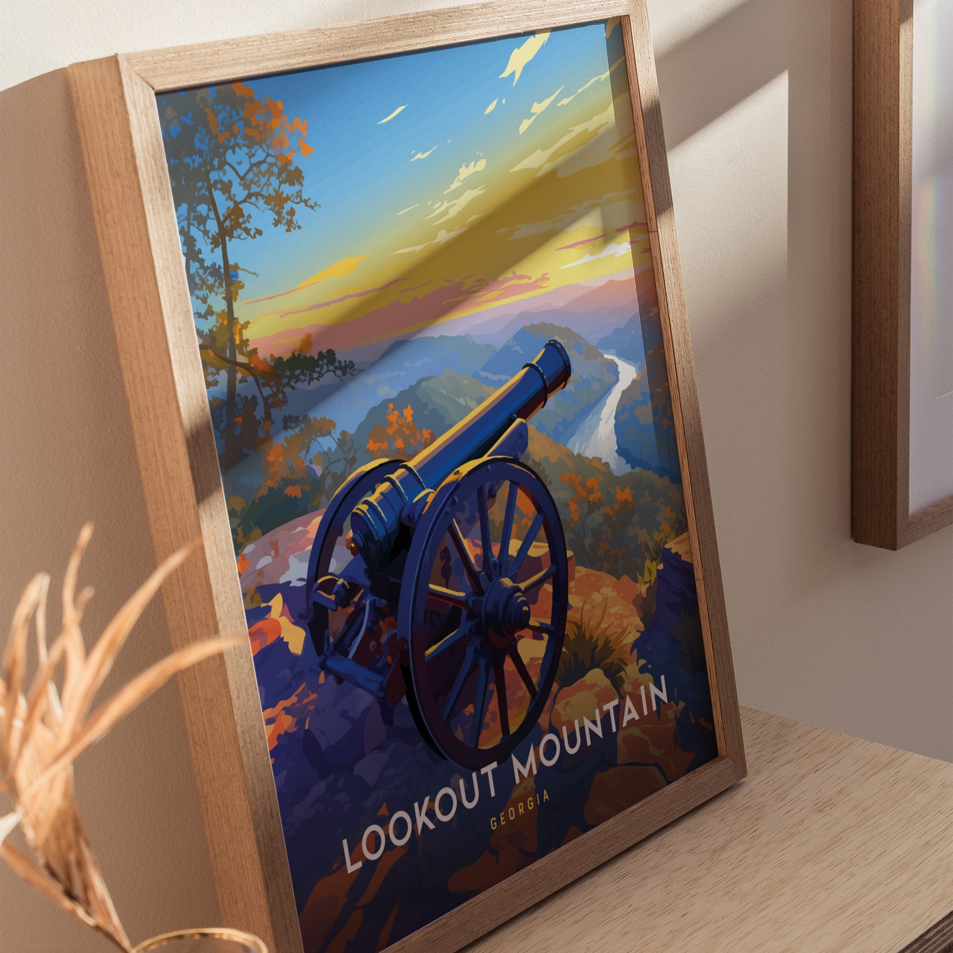 Framed poster of Lookout Mountain, Georgia, featuring a historic cannon overlooking a vibrant sunset and scenic landscape. The artwork is displayed on a wooden surface.