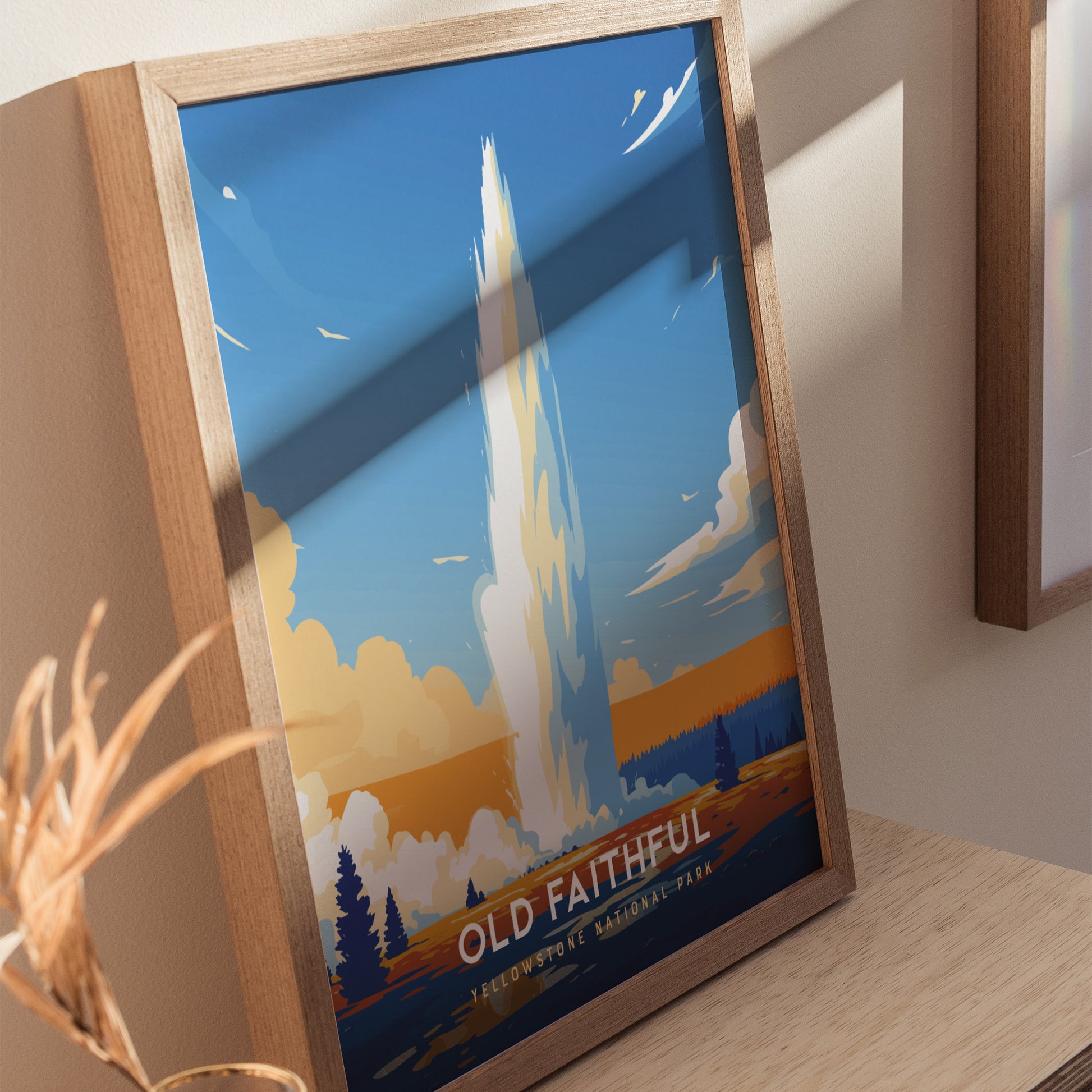 Framed Old Faithful Geyser poster featuring a stylized eruption against a vibrant blue sky with clouds, set on a wooden shelf.