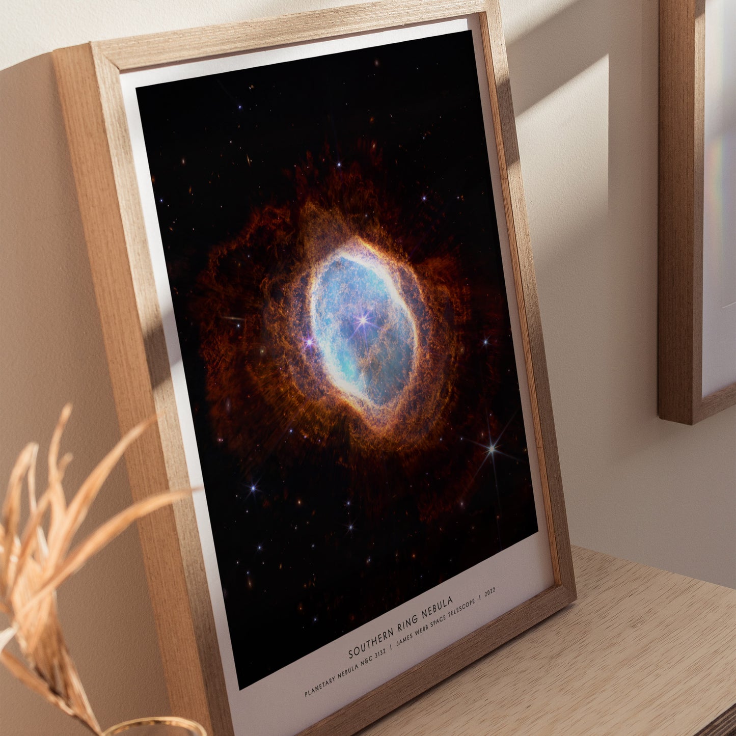 Natural wood framed Southern Ring Nebula space print leaning on a shelf beside plants and neutral accessories