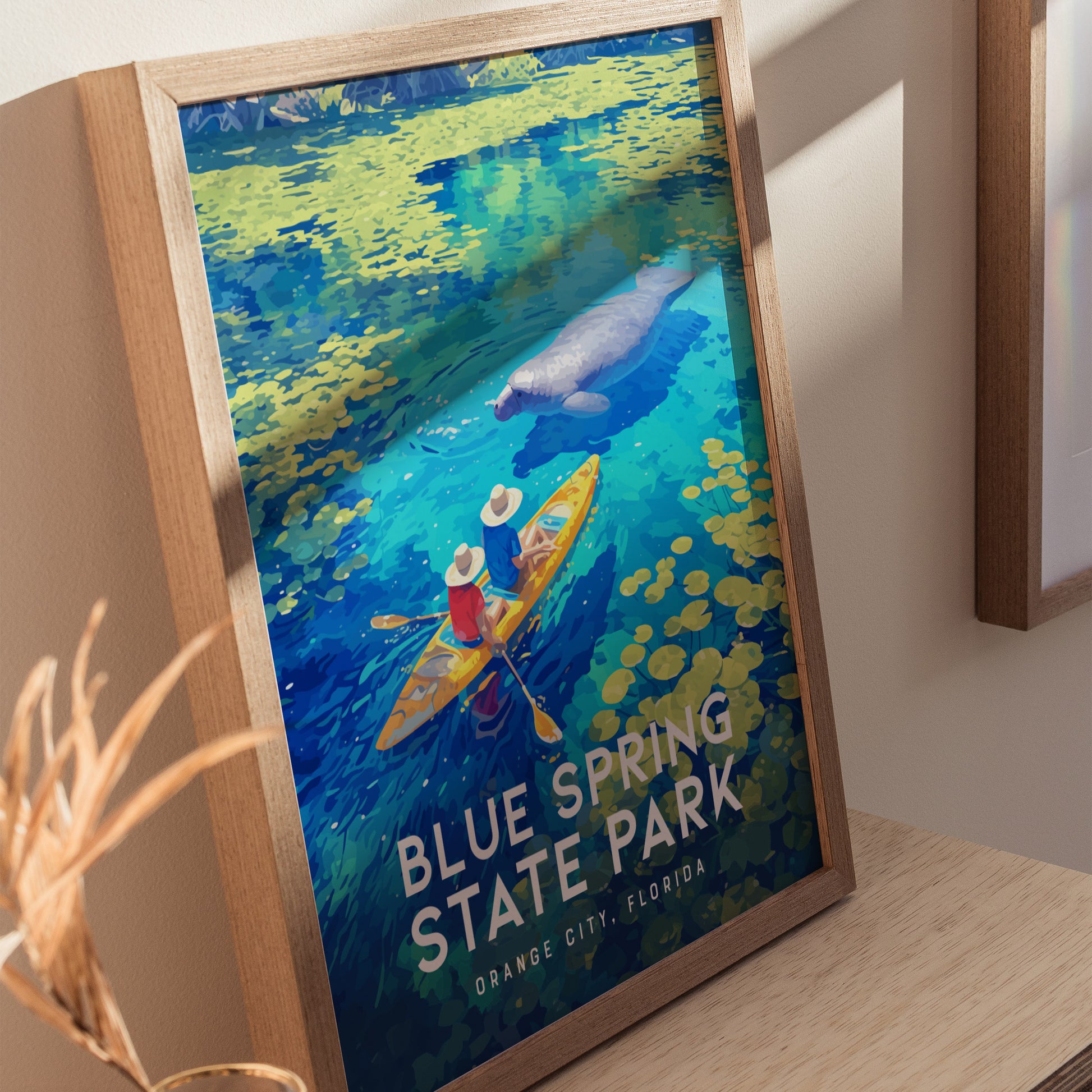 A framed poster depicts two kayakers in vibrant waters with a nearby manatee, surrounded by lush greenery. The text reads Blue Spring State Park, Orange City, Florida.