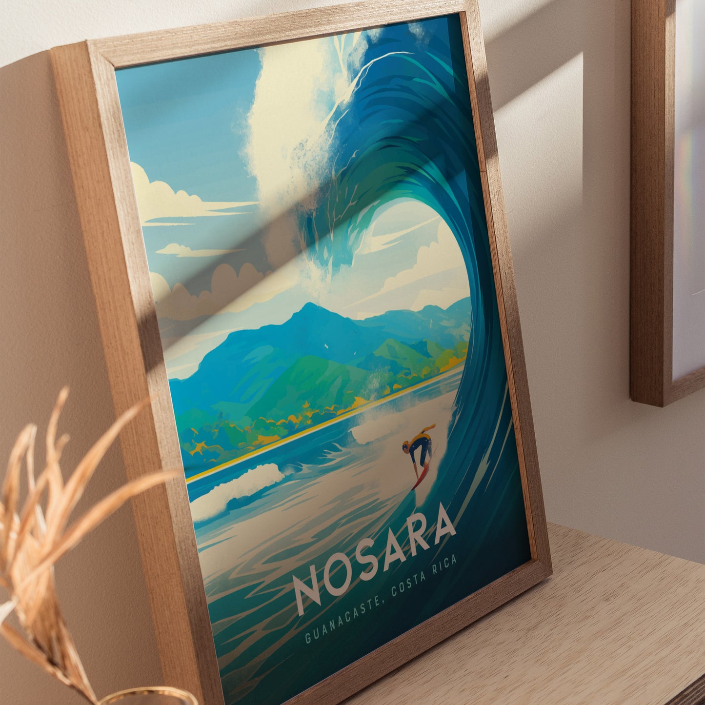 A framed poster of Nosara, Costa Rica, featuring an illustrated surfer riding a large wave with mountains in the background, displayed on a wooden surface.