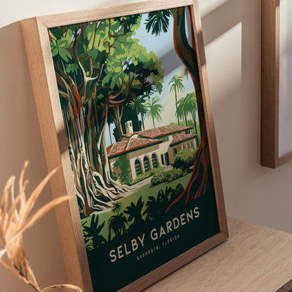 A framed poster of Selby Gardens in Sarasota, Florida, featuring lush greenery and a Mediterranean-style building, sits on a wooden surface with soft lighting.