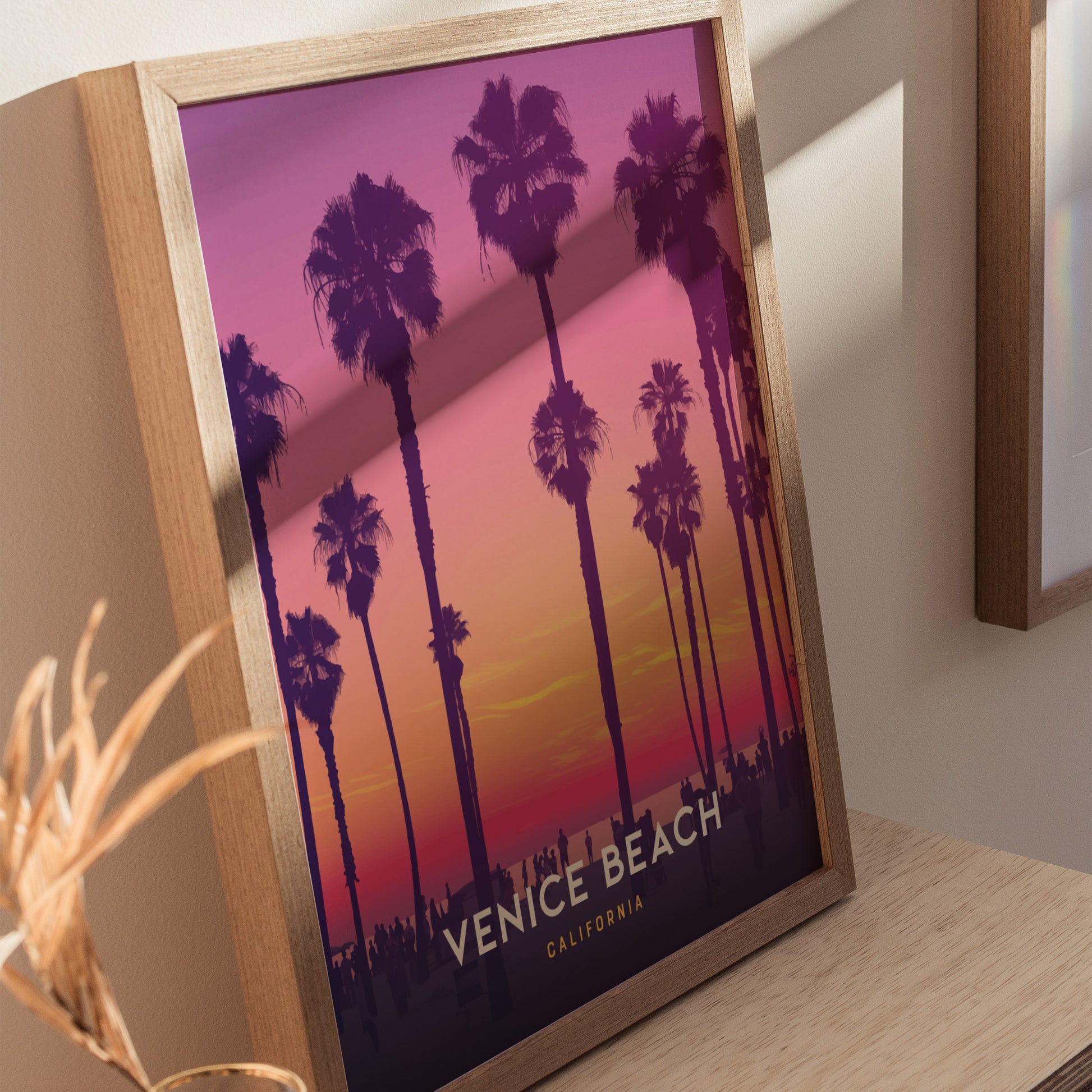 A framed poster featuring silhouetted palm trees against a vibrant sunset in shades of purple and orange, with Venice Beach California written at the bottom.
