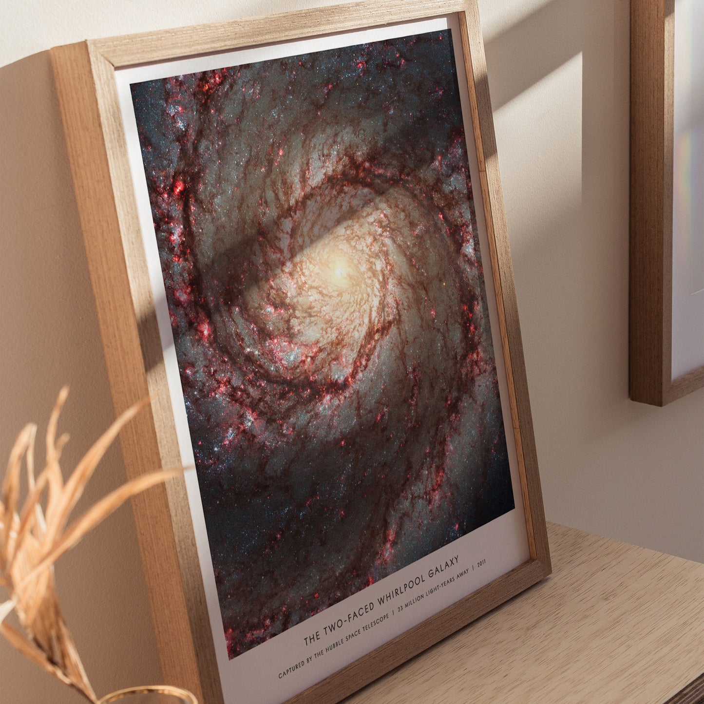 Natural wood framed Whirlpool Galaxy M51 space print leaning on a shelf next to plants and neutral accessories