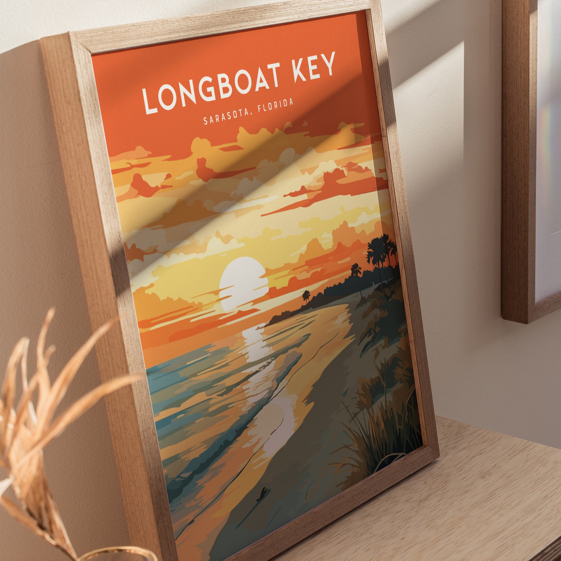 A framed poster displaying a vibrant sunset over a beach with sea oats and palm trees, labeled Longboat Key, Sarasota, Florida. The artwork features warm orange and yellow hues reflecting on the ocean.