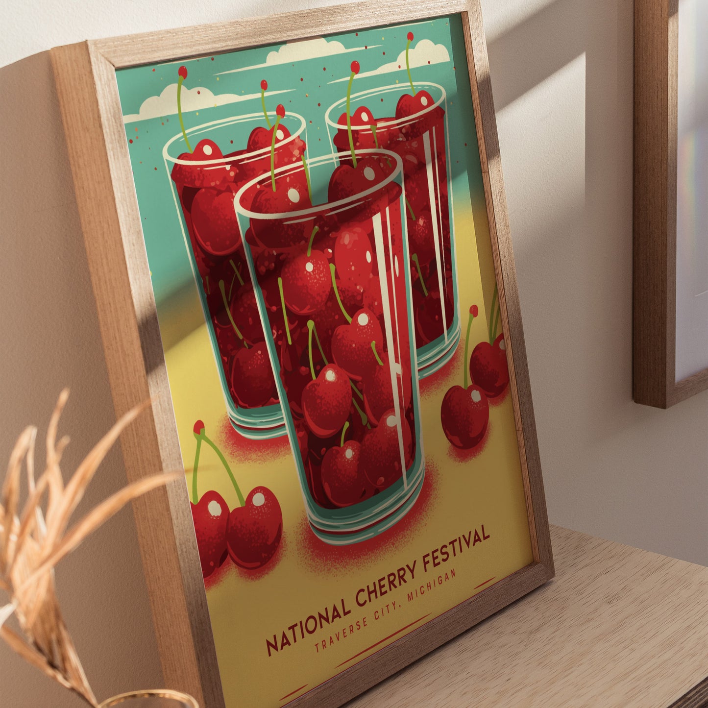 A framed poster featuring glasses filled with cherries against a vibrant yellow and turquoise background. The text reads National Cherry Festival, Traverse City, Michigan.