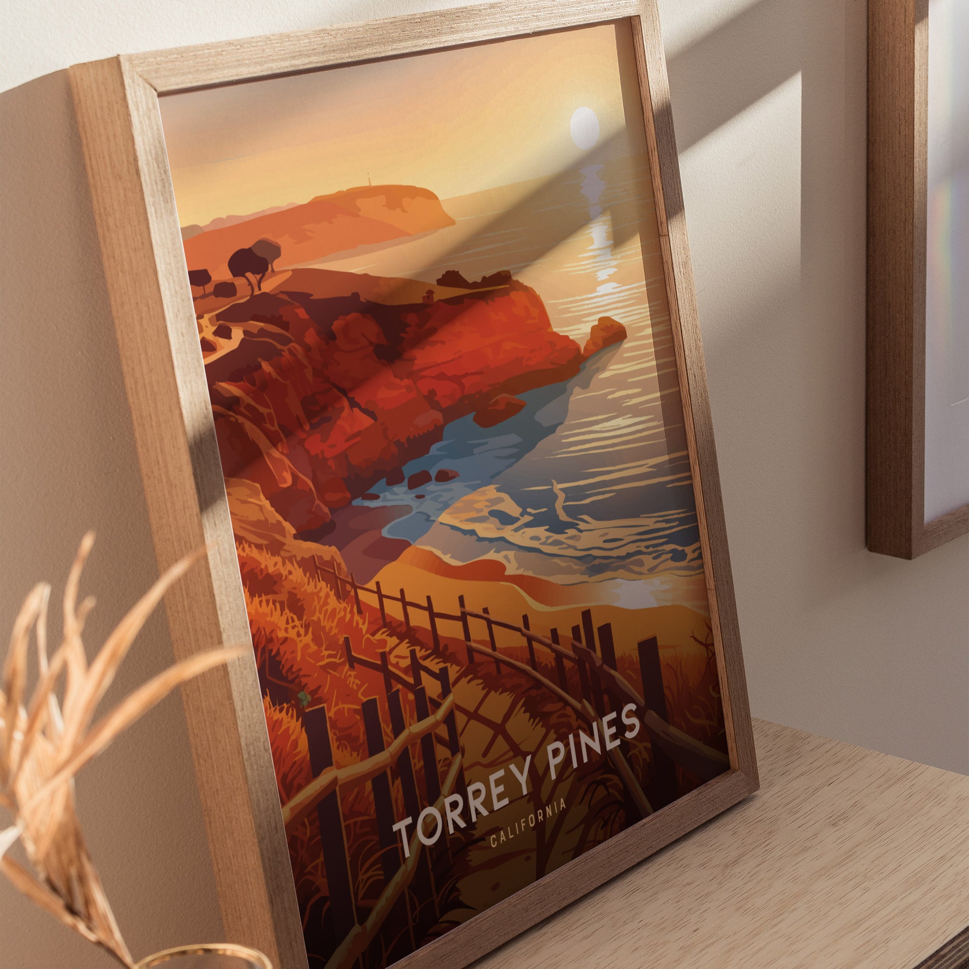 Framed artwork depicting Torrey Pines, California, features vibrant orange cliffs, a winding coastal trail, and a serene ocean view under a setting sun.