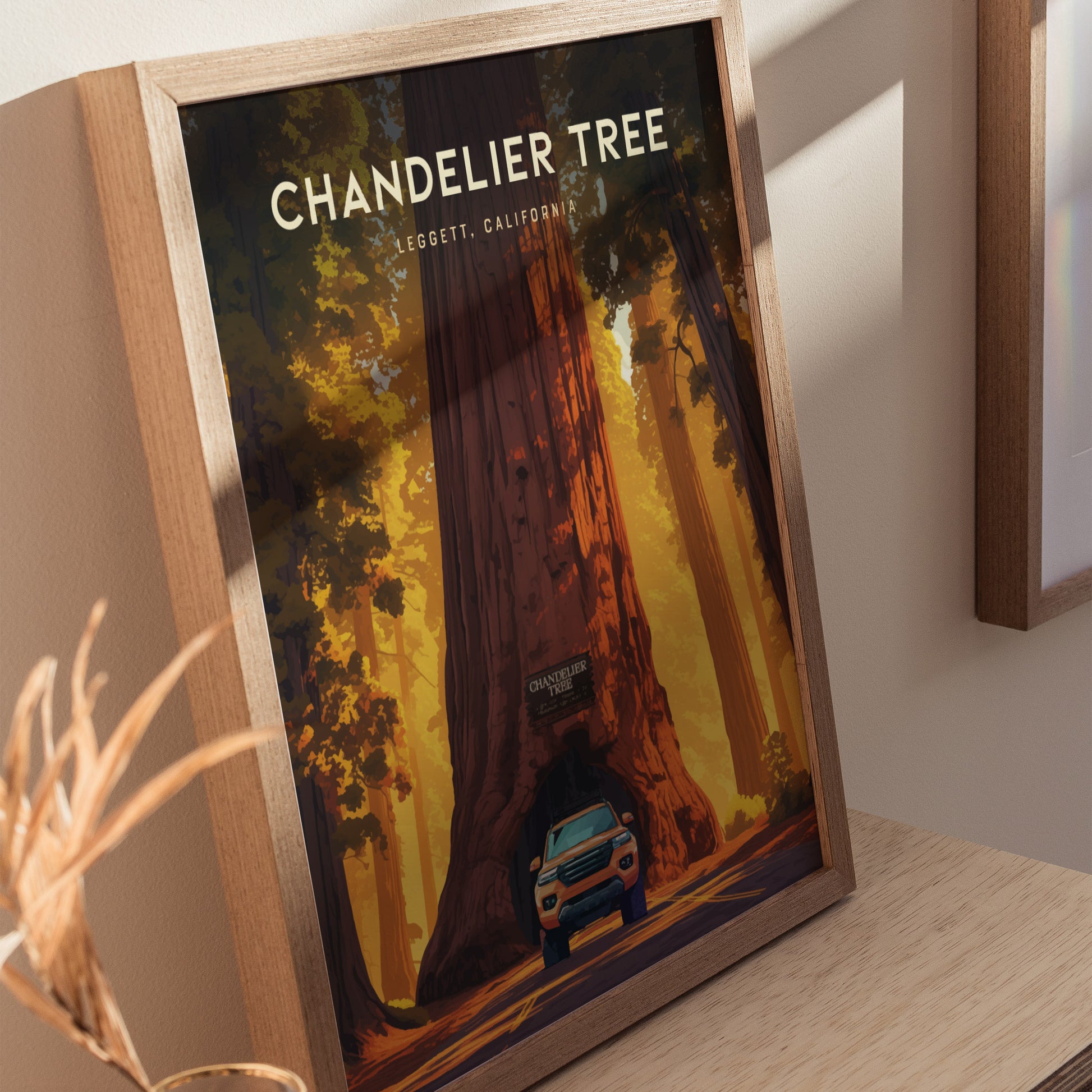 Framed poster of the Chandelier Tree in Leggett, California, depicting a car driving through the tunnel carved in the massive redwood. Warm sunlight filters through the forest canopy.
