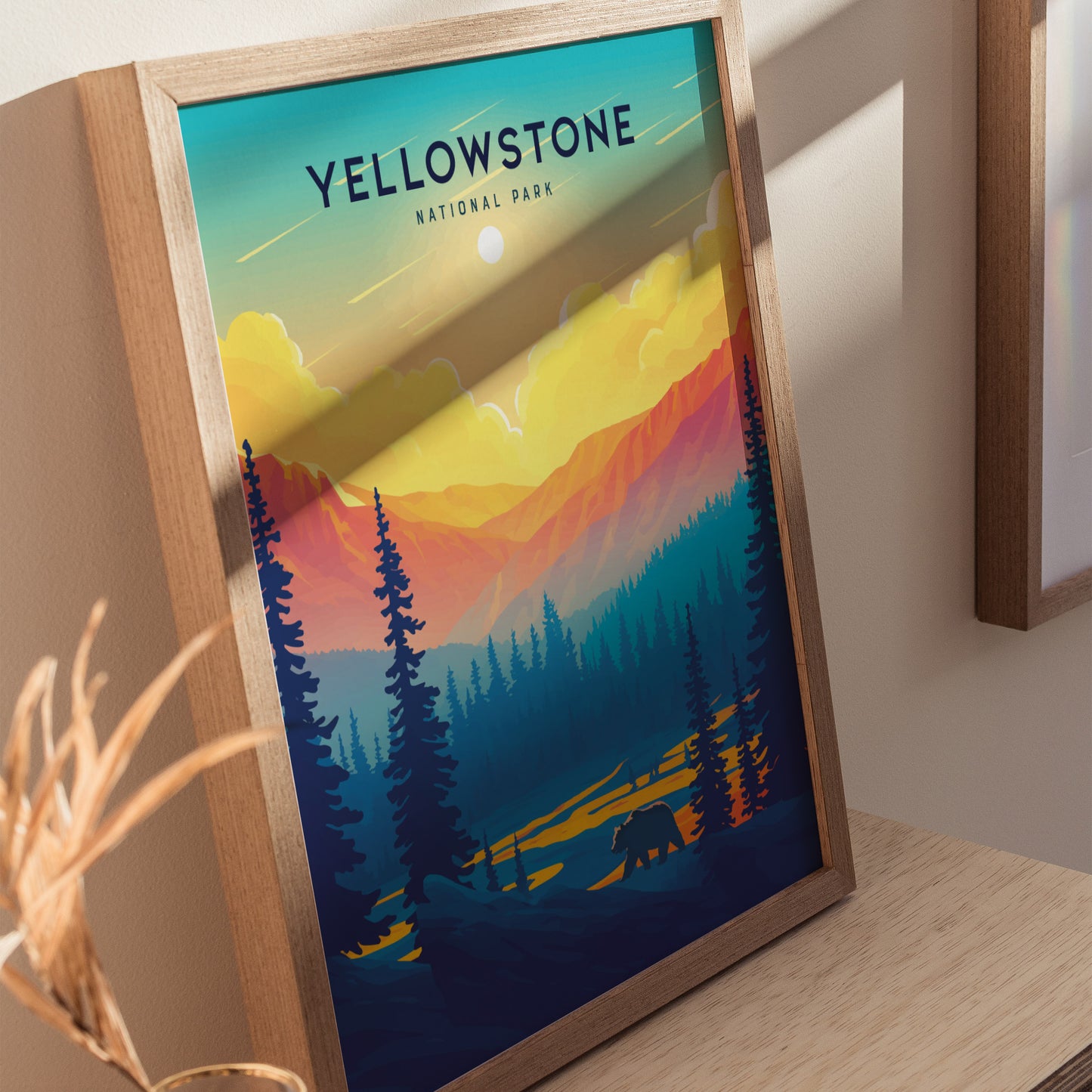 Framed Yellowstone National Park poster featuring a vibrant sunset with silhouettes of pine trees and a bear against colorful mountains. The artwork is set on a light wooden surface.