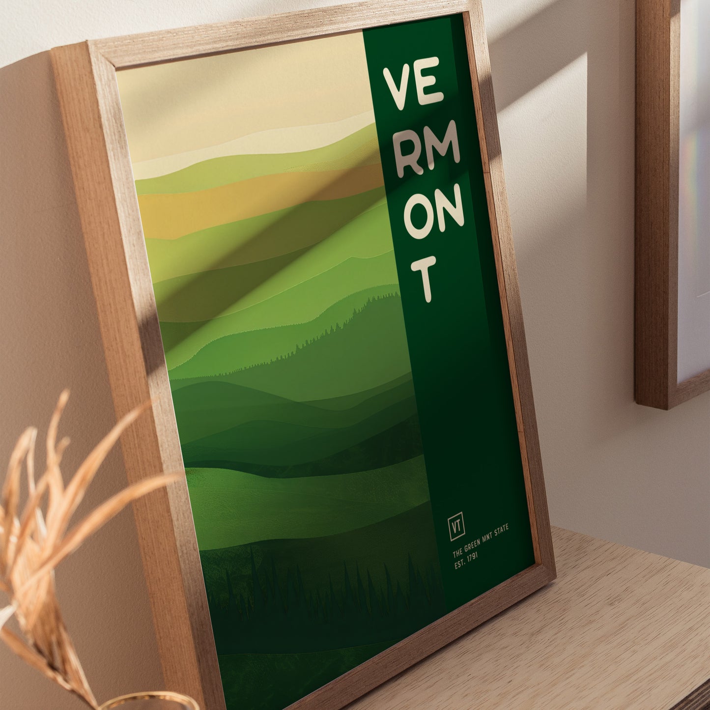 Framed poster featuring a minimalist design of rolling green hills and the word Vermont in bold letters on the right. The artwork evokes the natural beauty of Vermont.