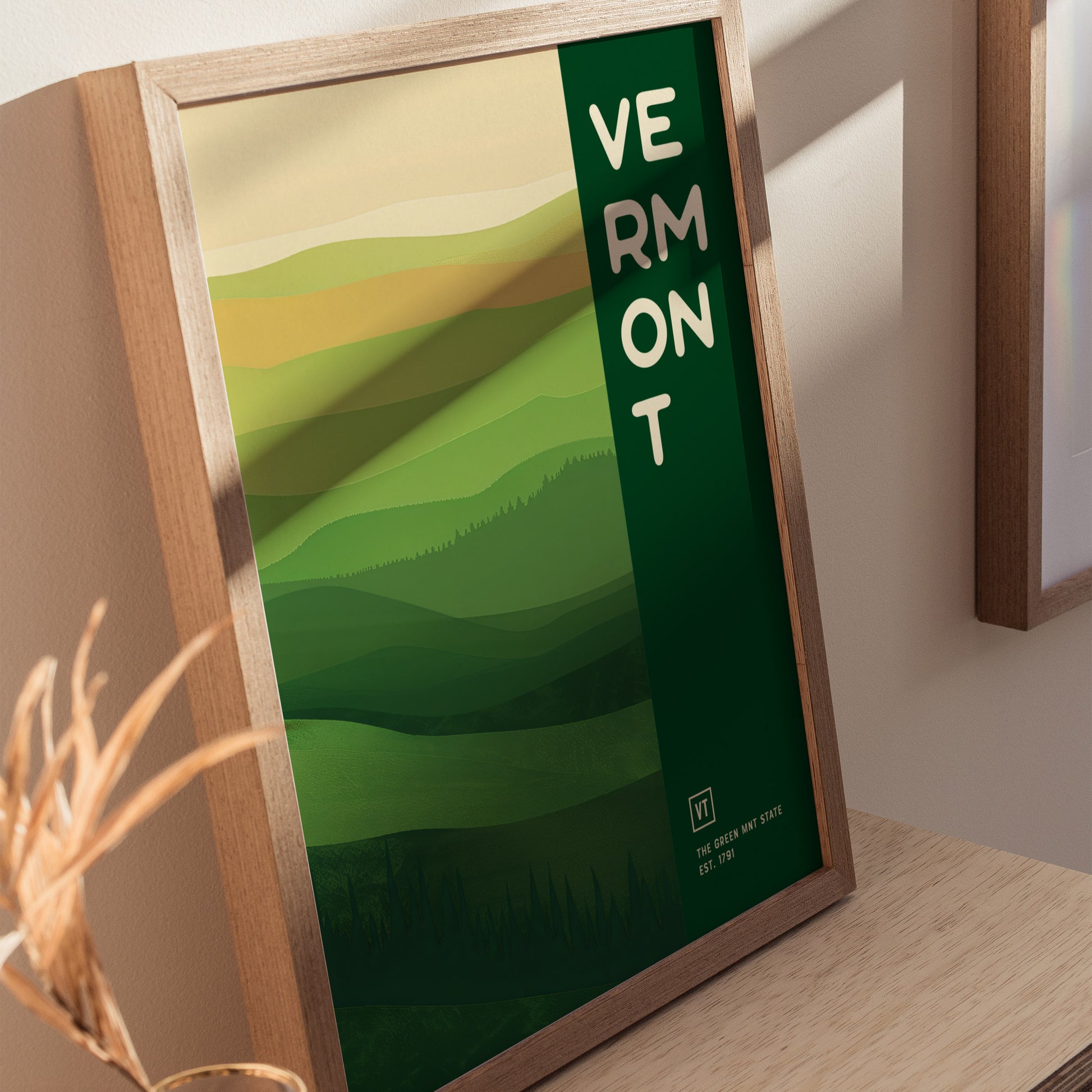 Framed poster featuring a minimalist design of rolling green hills and the word Vermont in bold letters on the right. The artwork evokes the natural beauty of Vermont.