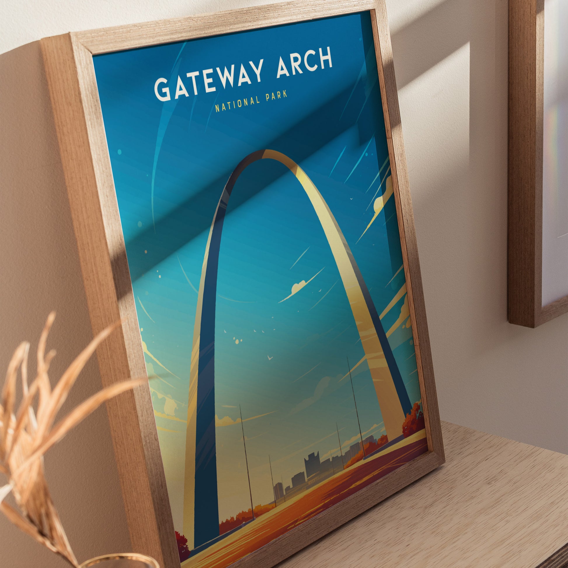 Framed poster of the Gateway Arch in St. Louis, featuring a minimalist design against a clear blue sky, displayed on a wooden surface.