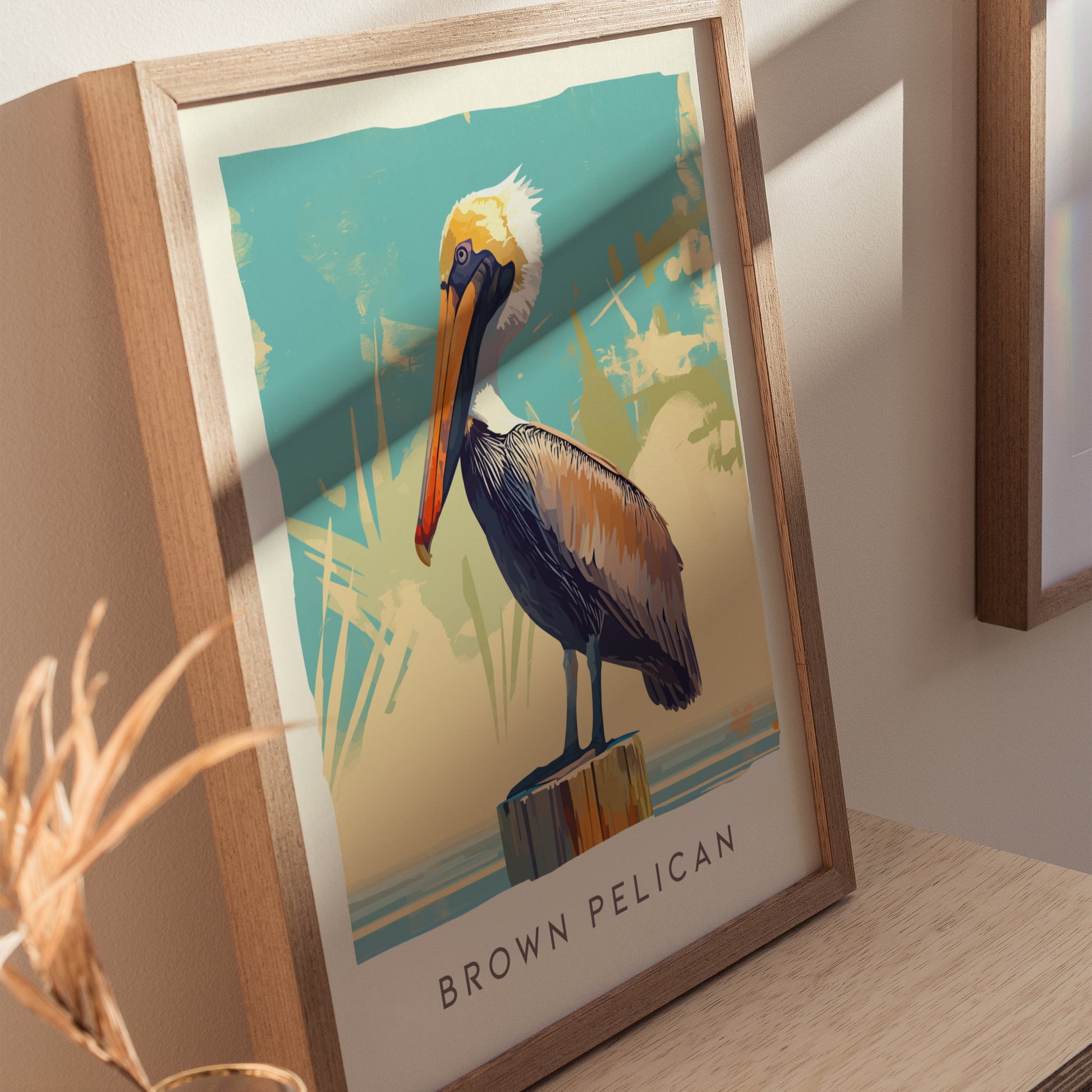 A framed poster featuring a stylized illustration of a Brown Pelican perched on a post against a blue and beige abstract background, displayed on a wooden surface.