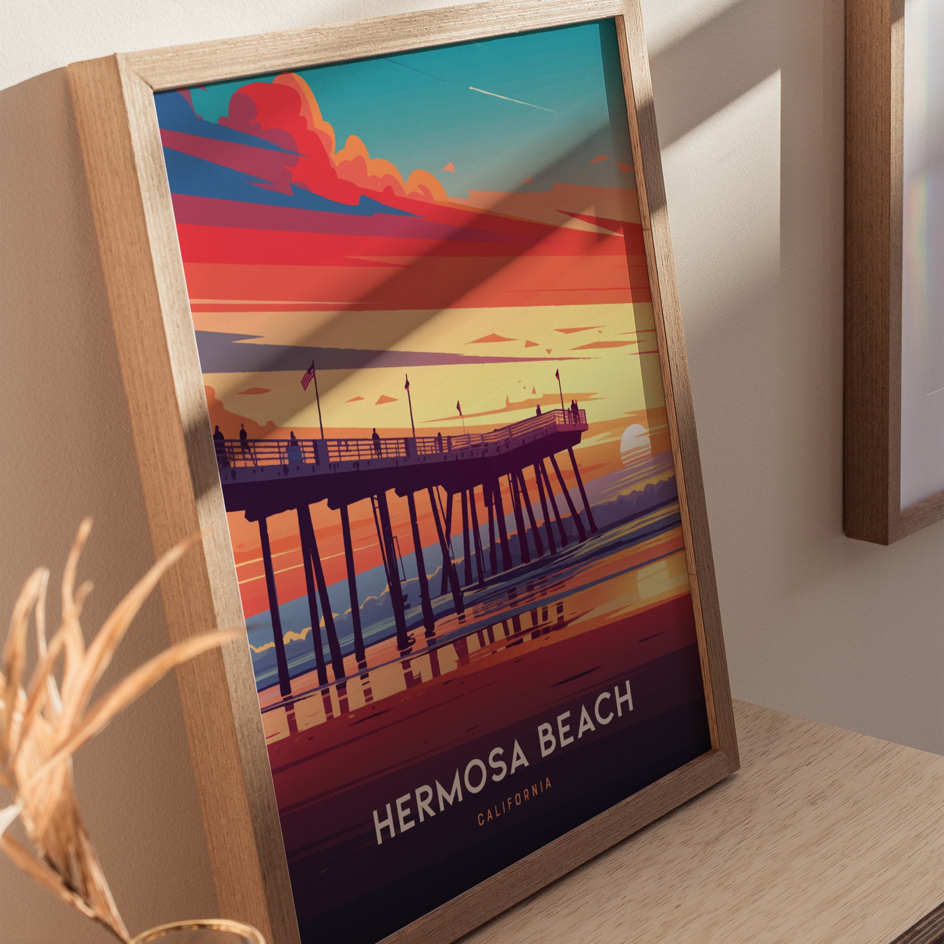 Framed artwork of Hermosa Beach Pier at sunset, featuring vibrant orange, pink, and blue hues. The image captures a serene coastal scene with silhouetted figures on the pier.